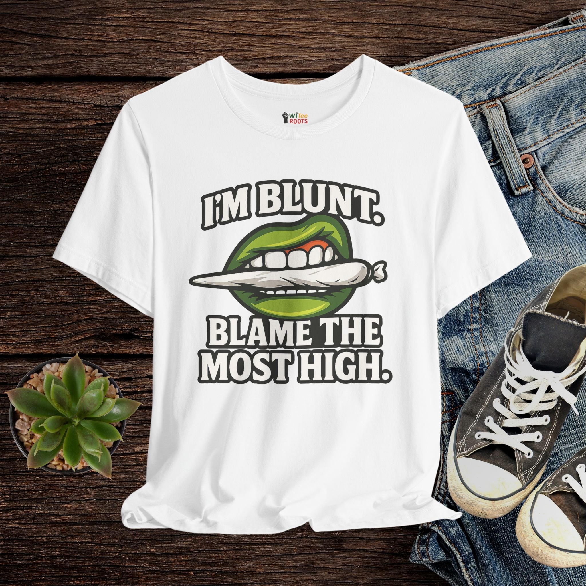White t-shirt with graphic design and text on a wooden surface with jeans and sneakers.