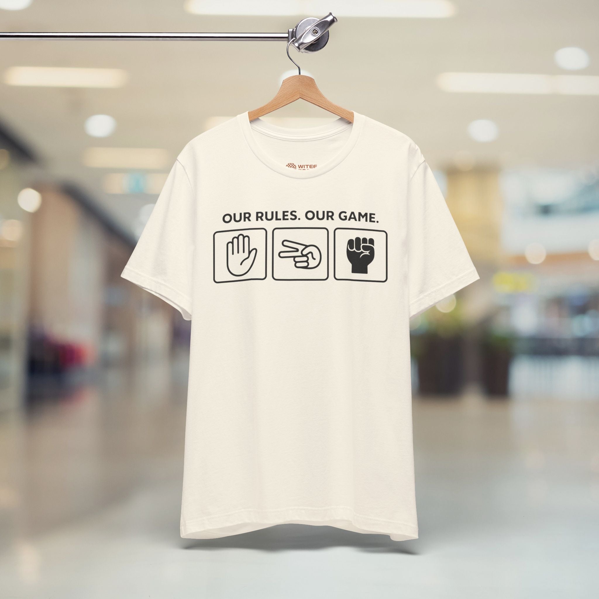 Beige t-shirt with text and symbols on a hanger in a blurred indoor setting