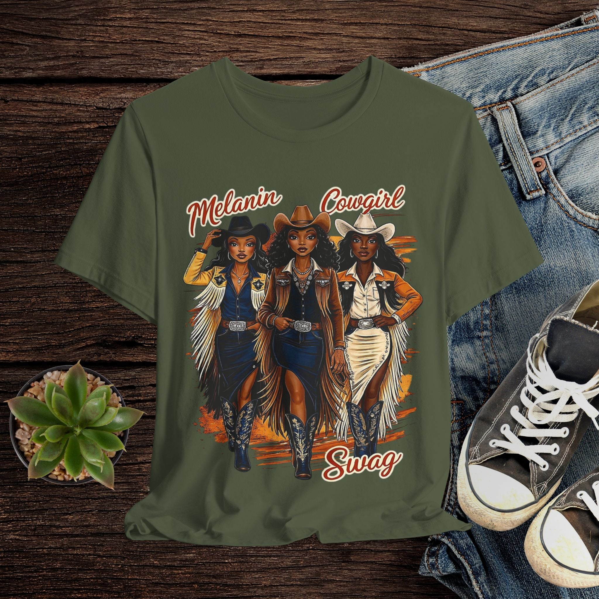 Green t-shirt with cowgirl graphic and text on a wooden surface with jeans and sneakers.