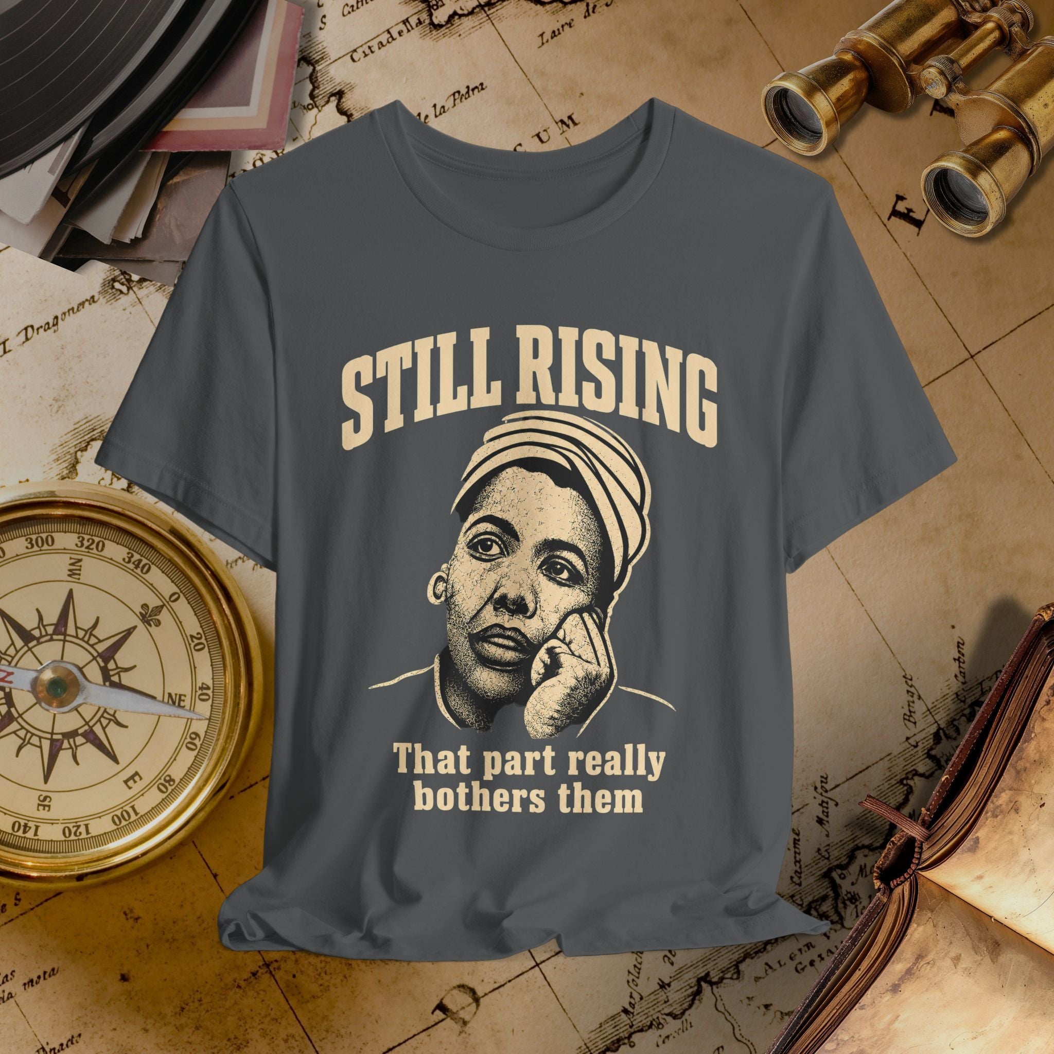 T-shirt with a graphic of a person and text 'STILL RISING That part really bothers them' on an old map background.