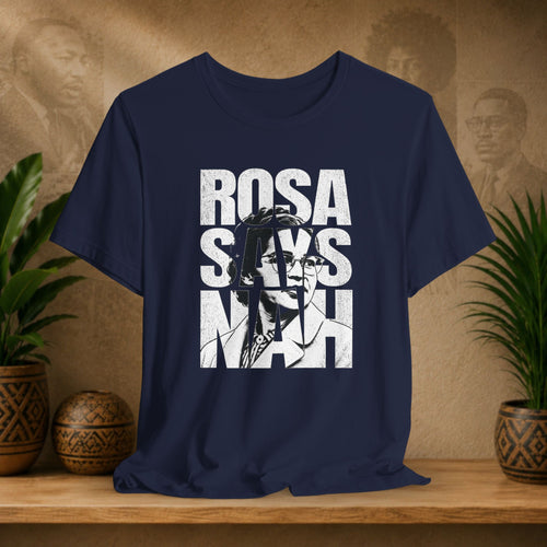 Navy blue t-shirt with 'Rosa Parks' graphic and text on a wooden surface with plants and a textured wall background.