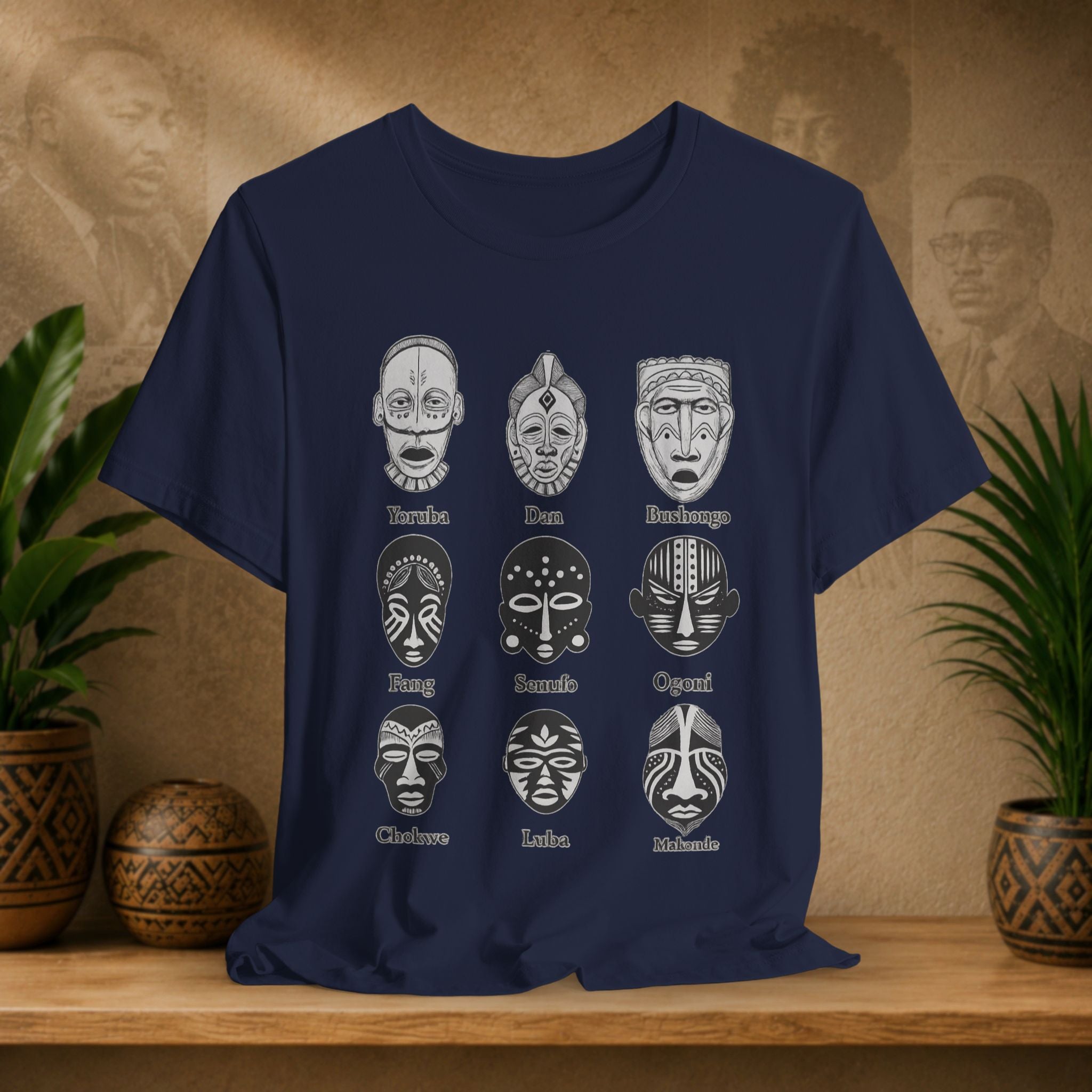 Navy blue t-shirt with white tribal mask designs on a wooden surface with plants and decorative items.