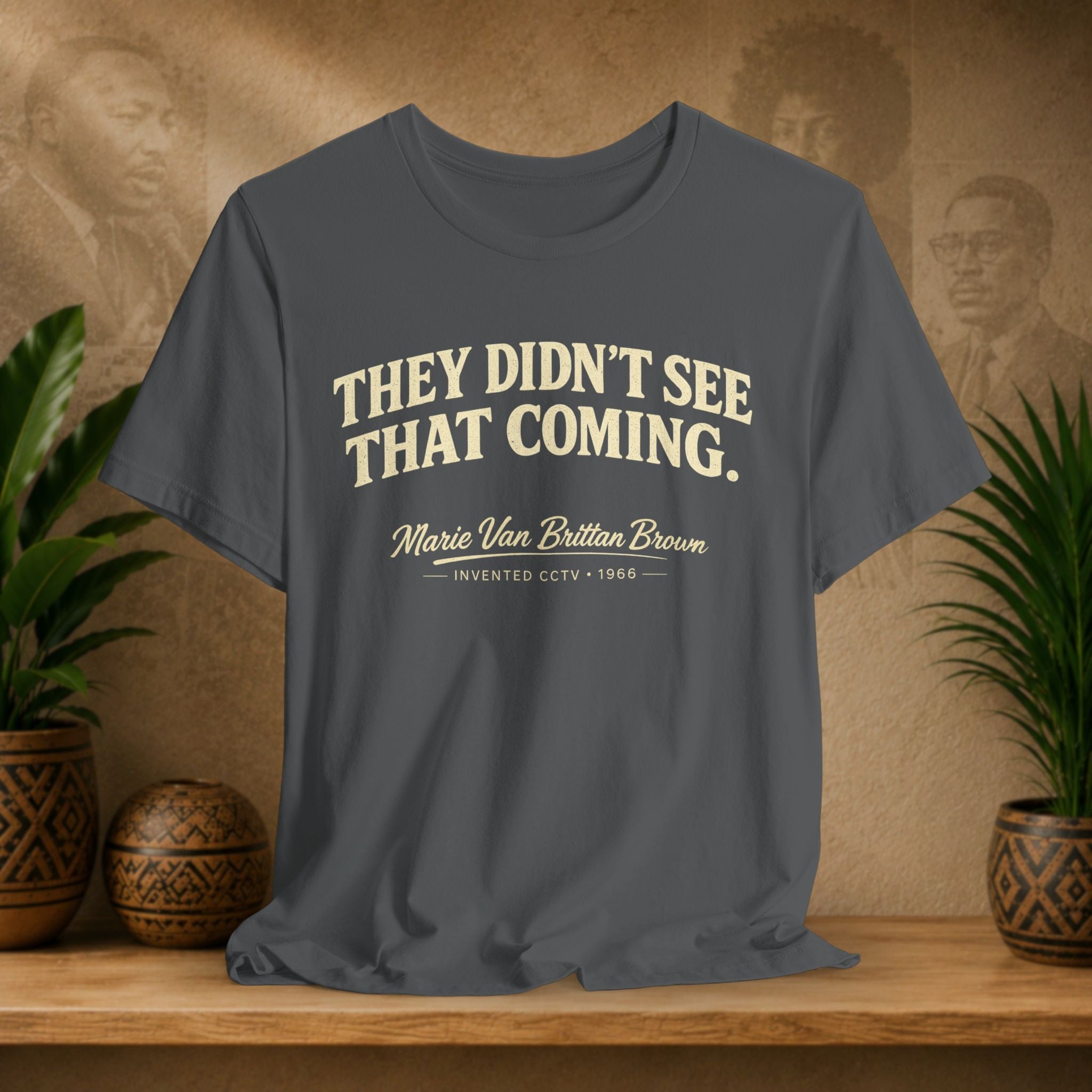 Gray t-shirt with text on a wooden surface with plants and a decorative wall in the background