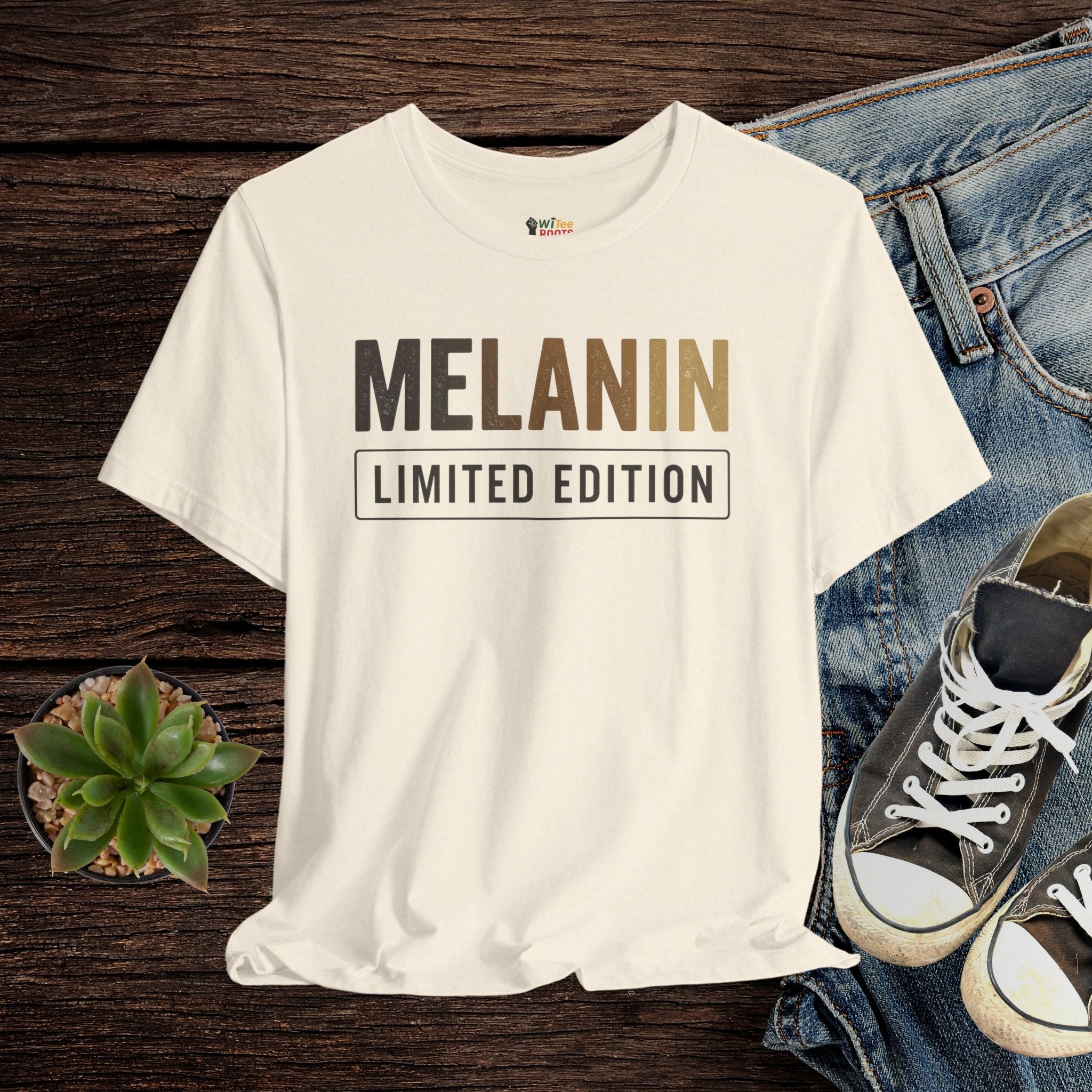 Cream t-shirt with 'MELANIN LIMITED EDITION' text on a wooden surface with jeans and sneakers.