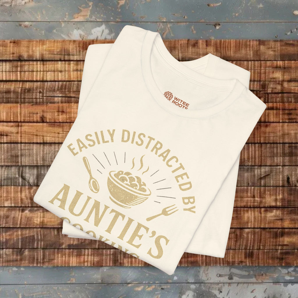 Beige t-shirt with gold text and graphics on a wooden surface