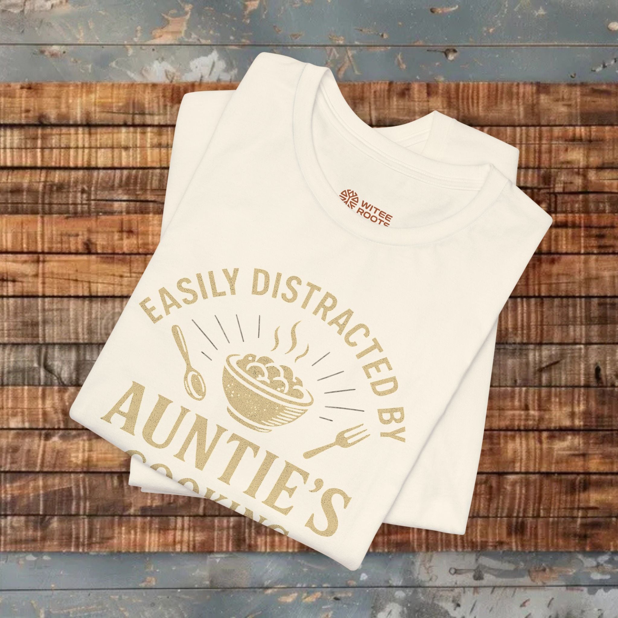 Beige t-shirt with gold text and graphics on a wooden surface