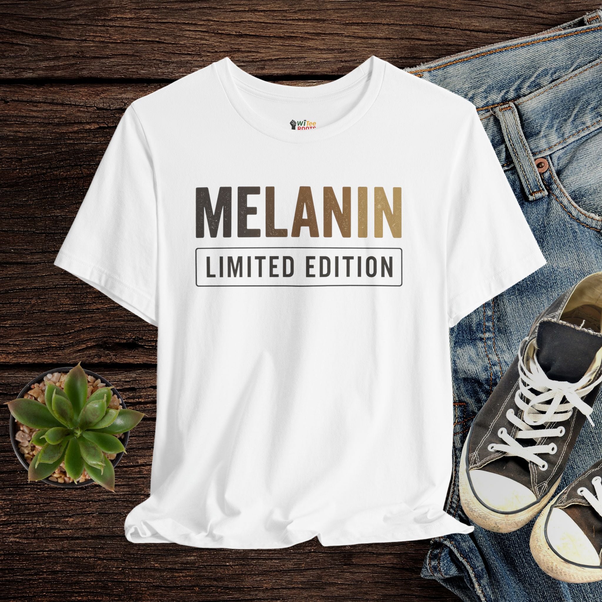 White t-shirt with 'MELANIN LIMITED EDITION' text on a wooden surface with jeans and sneakers.