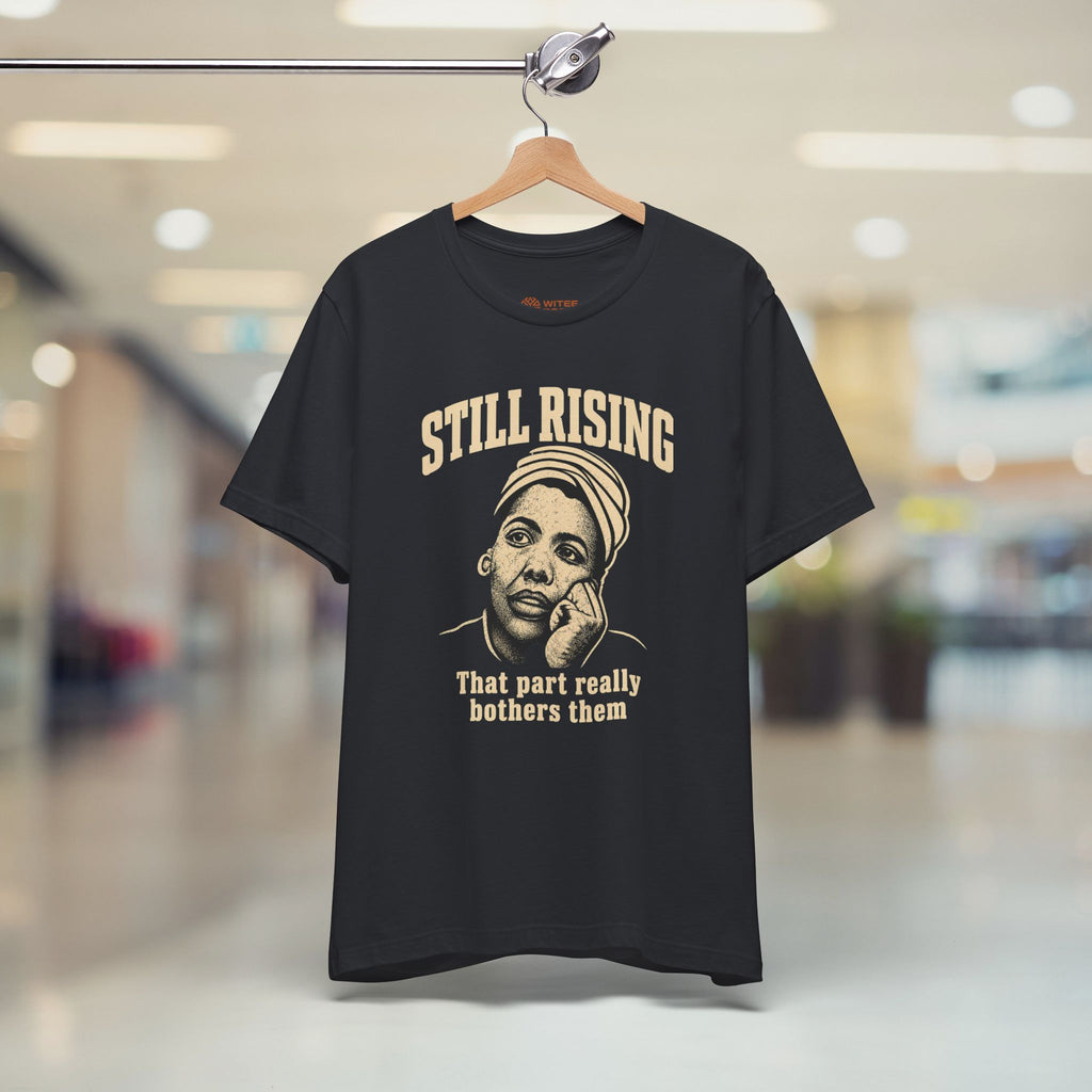 Black t-shirt with 'Still Rising' graphic and text on a hanger in a store setting