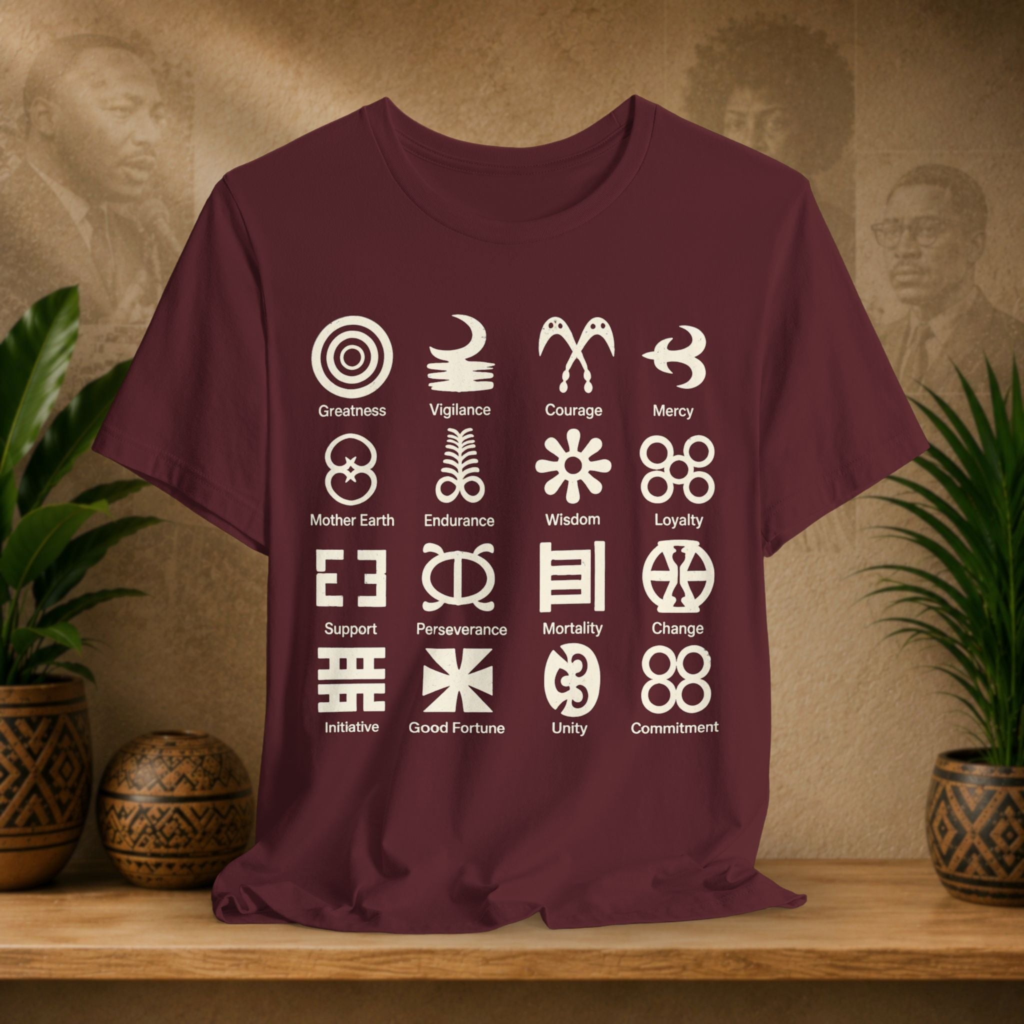 Maroon t-shirt with white symbols and text on a wooden surface with a decorative background