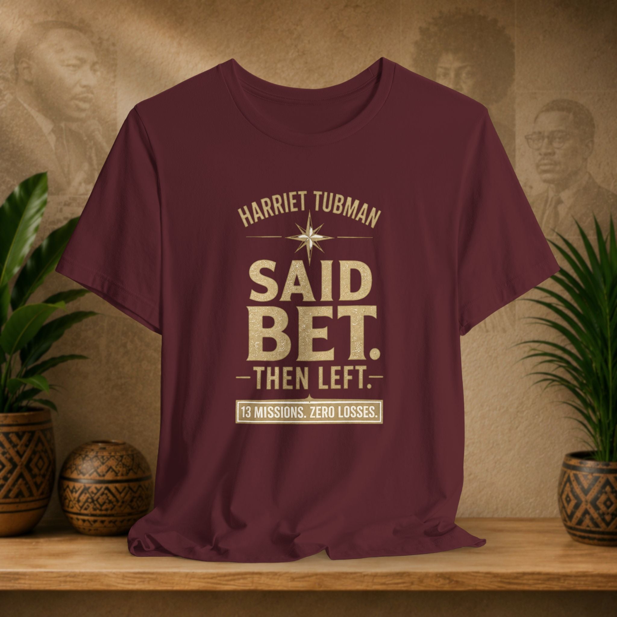 Maroon t-shirt with text design on a wooden surface with plants and wall art in the background