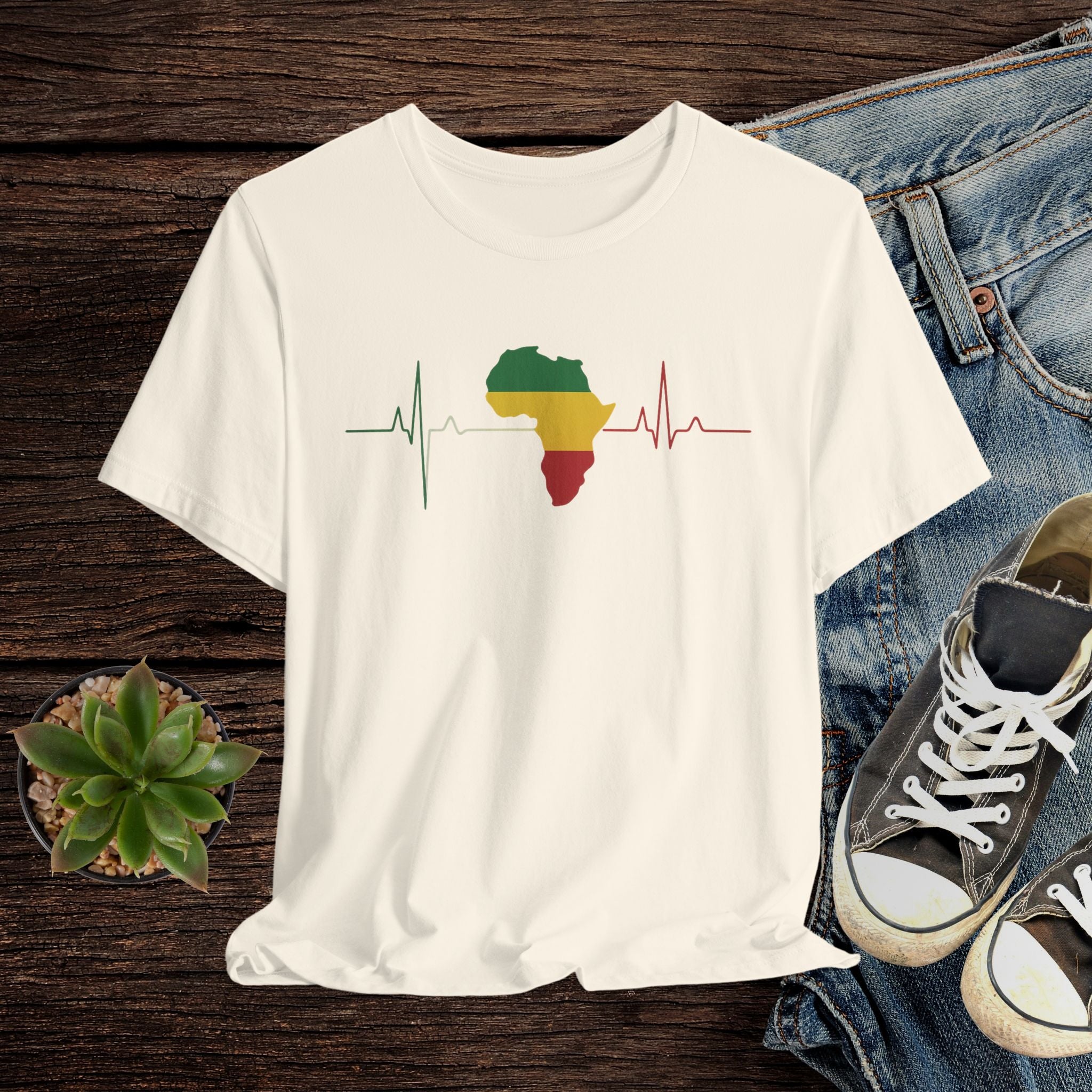 Beige t-shirt with a colorful Africa map design on a wooden surface with jeans and sneakers.