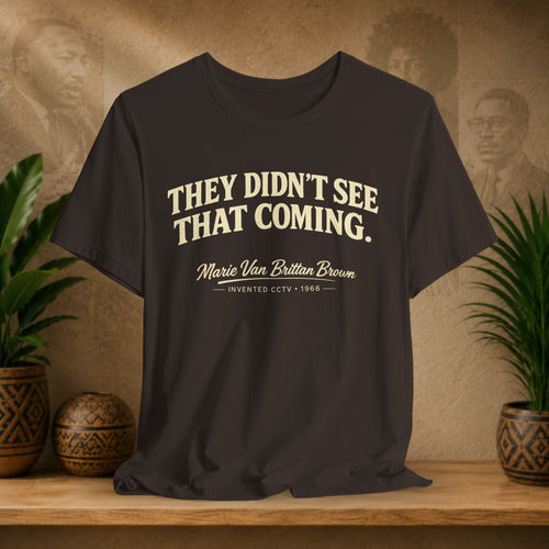 Brown t-shirt with text on a wooden surface with decorative plants and a vintage-style wall background.