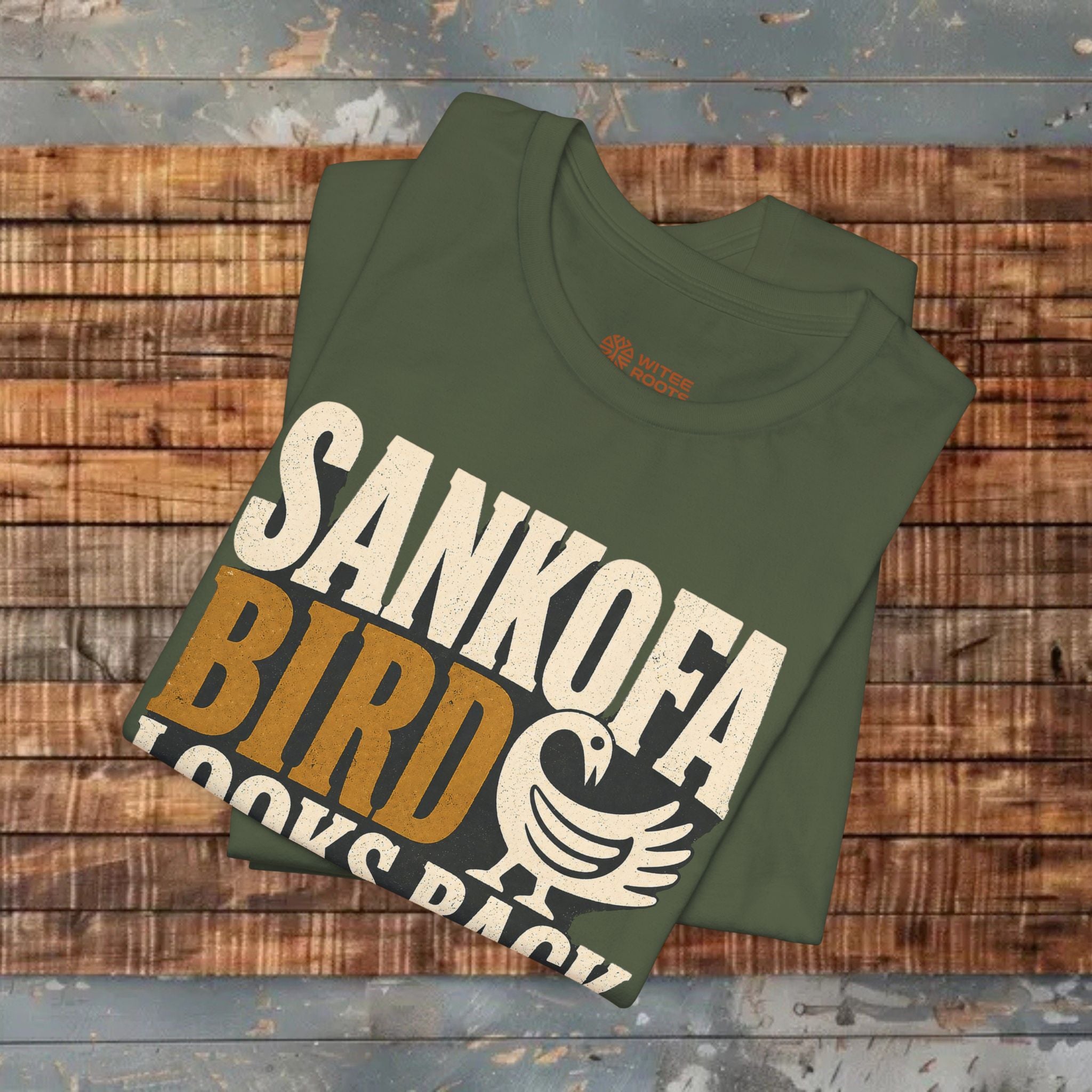 Green t-shirt with 'Sankofa Bird' text and logo on a wooden surface