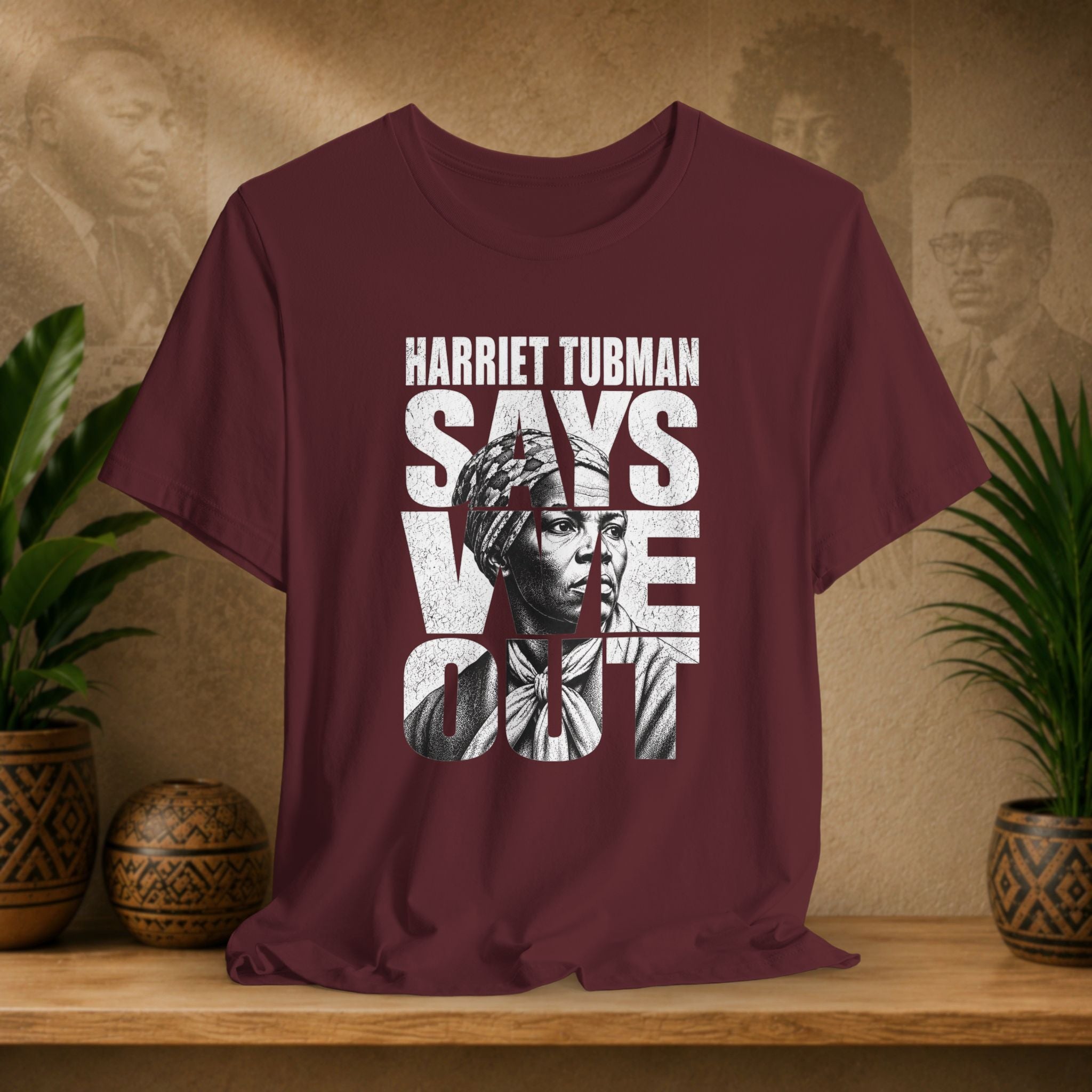 Maroon t-shirt with Harriet Tubman graphic and text on a wooden surface with plants and decorative items.