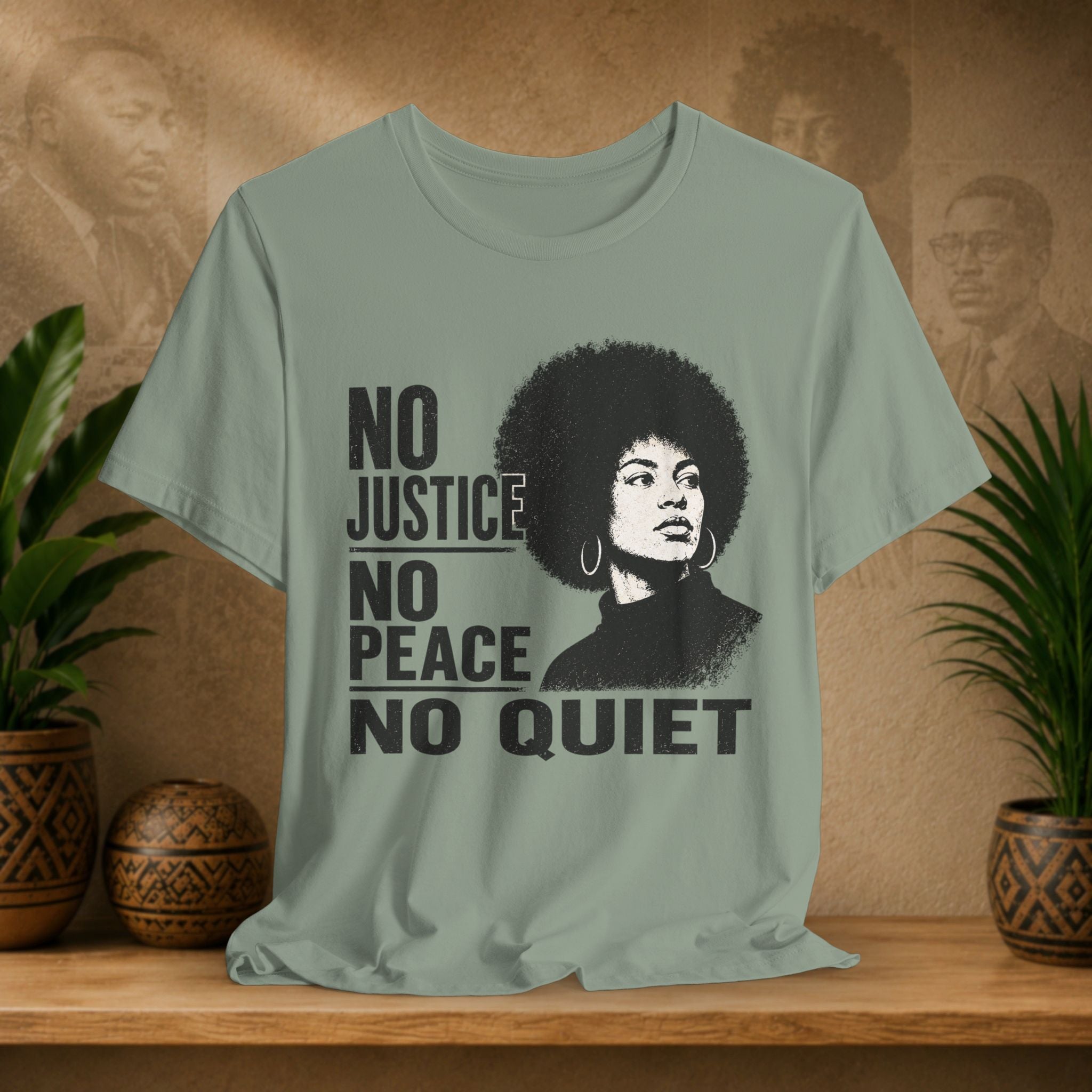 Sage green t-shirt with graphic and text on a wooden surface with plants and a textured wall background
