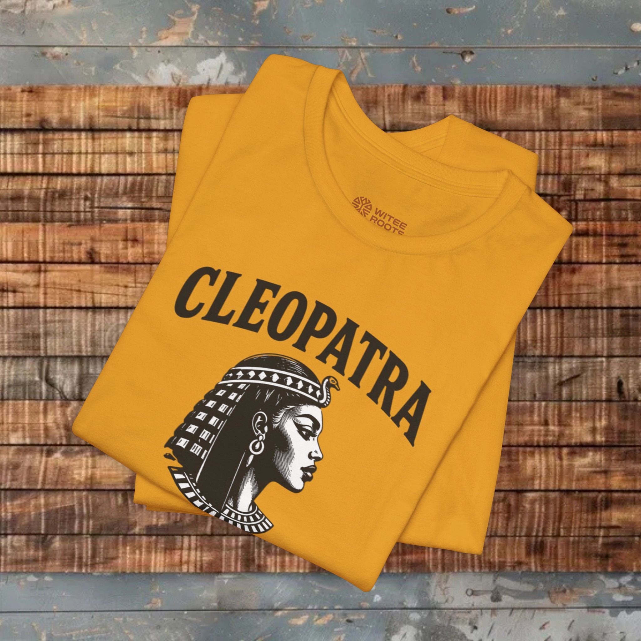 Mustard t-shirt with Cleopatra design on a wooden surface