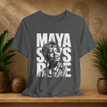 Gray t-shirt with 'Maya Says Rise' design on a wooden surface with plants and decorative items.