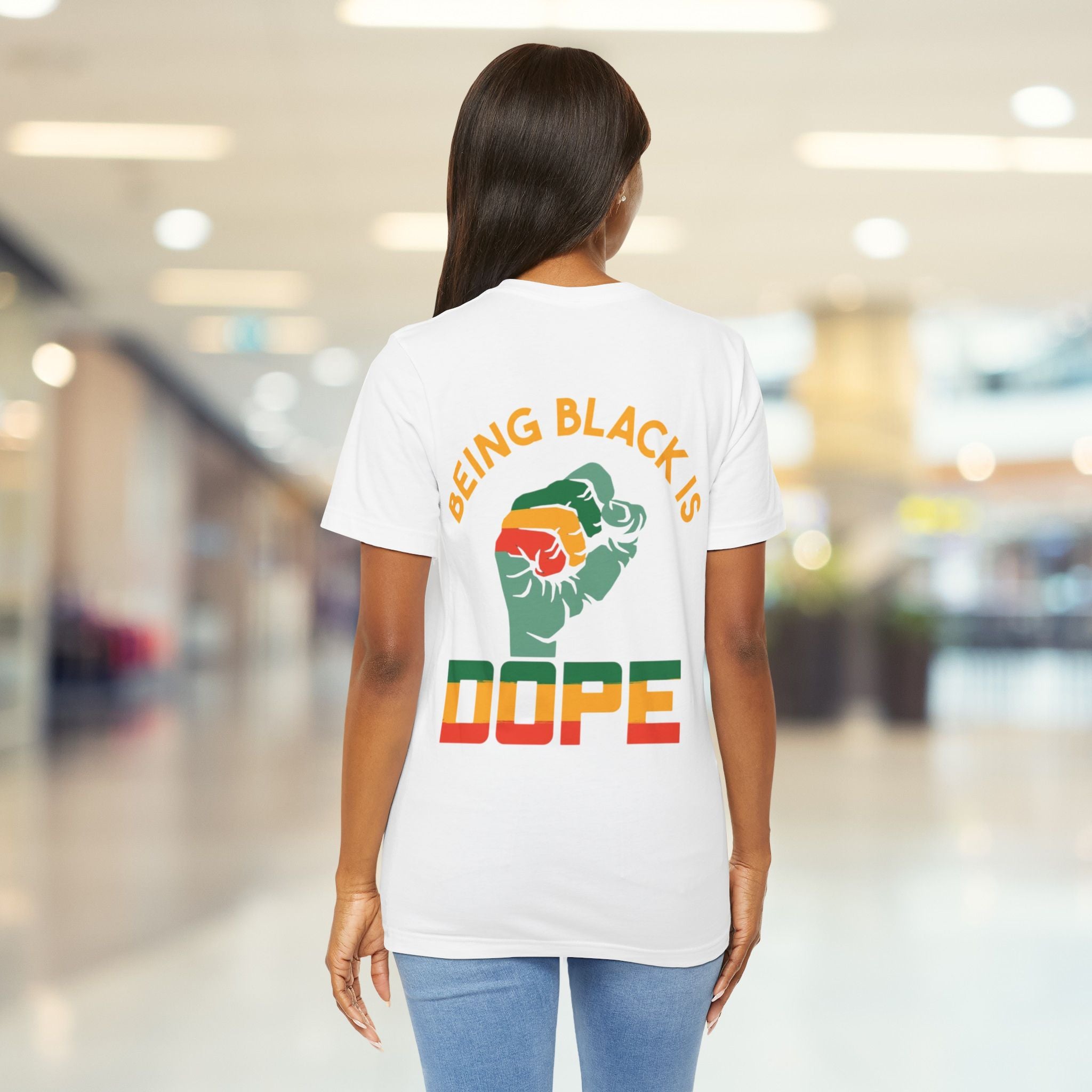 Person wearing a white t-shirt with a colorful graphic and text in a mall.