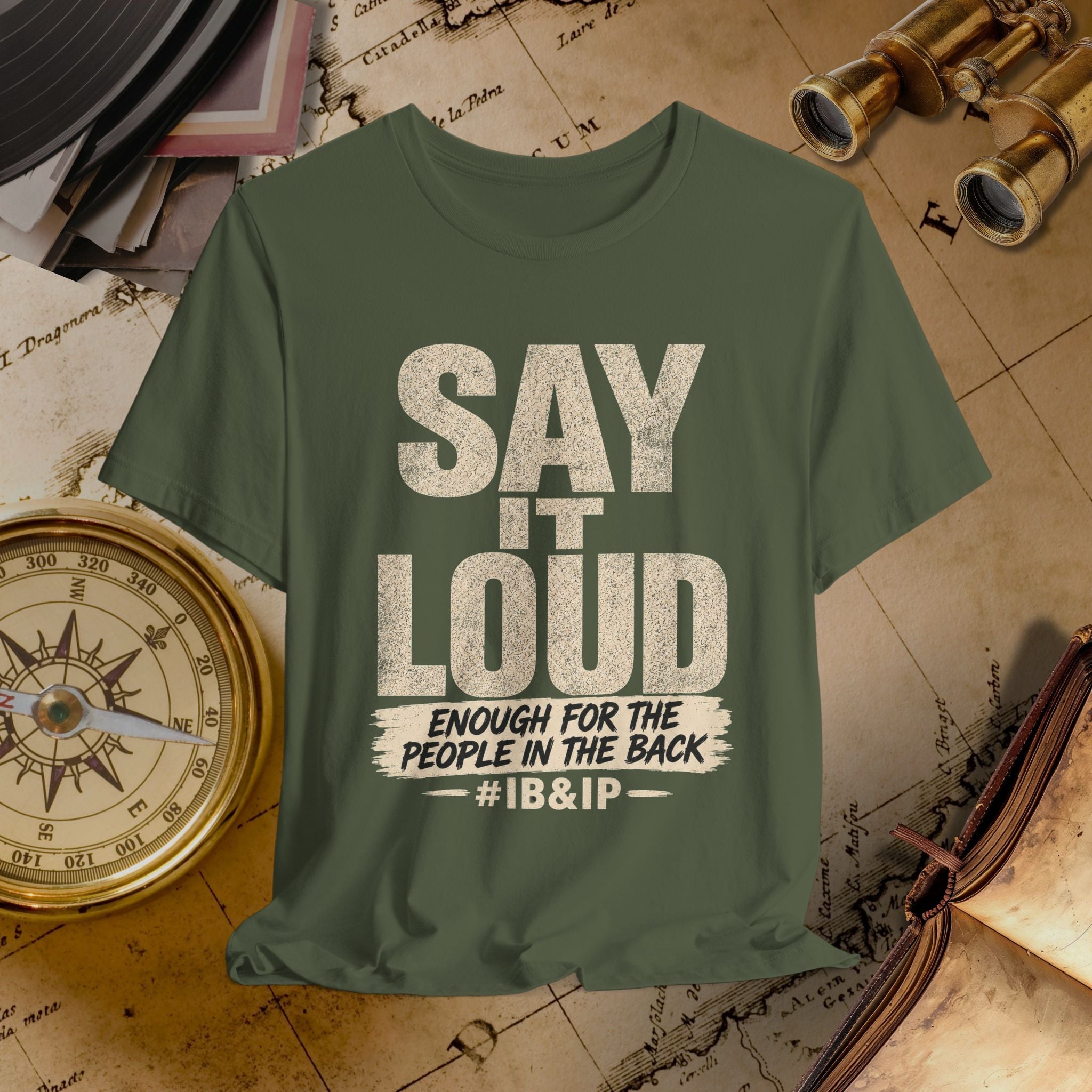 Green t-shirt with text 'SAY IT LOUD ENOUGH FOR THE PEOPLE IN THE BACK #IB&IP' on a vintage map background.