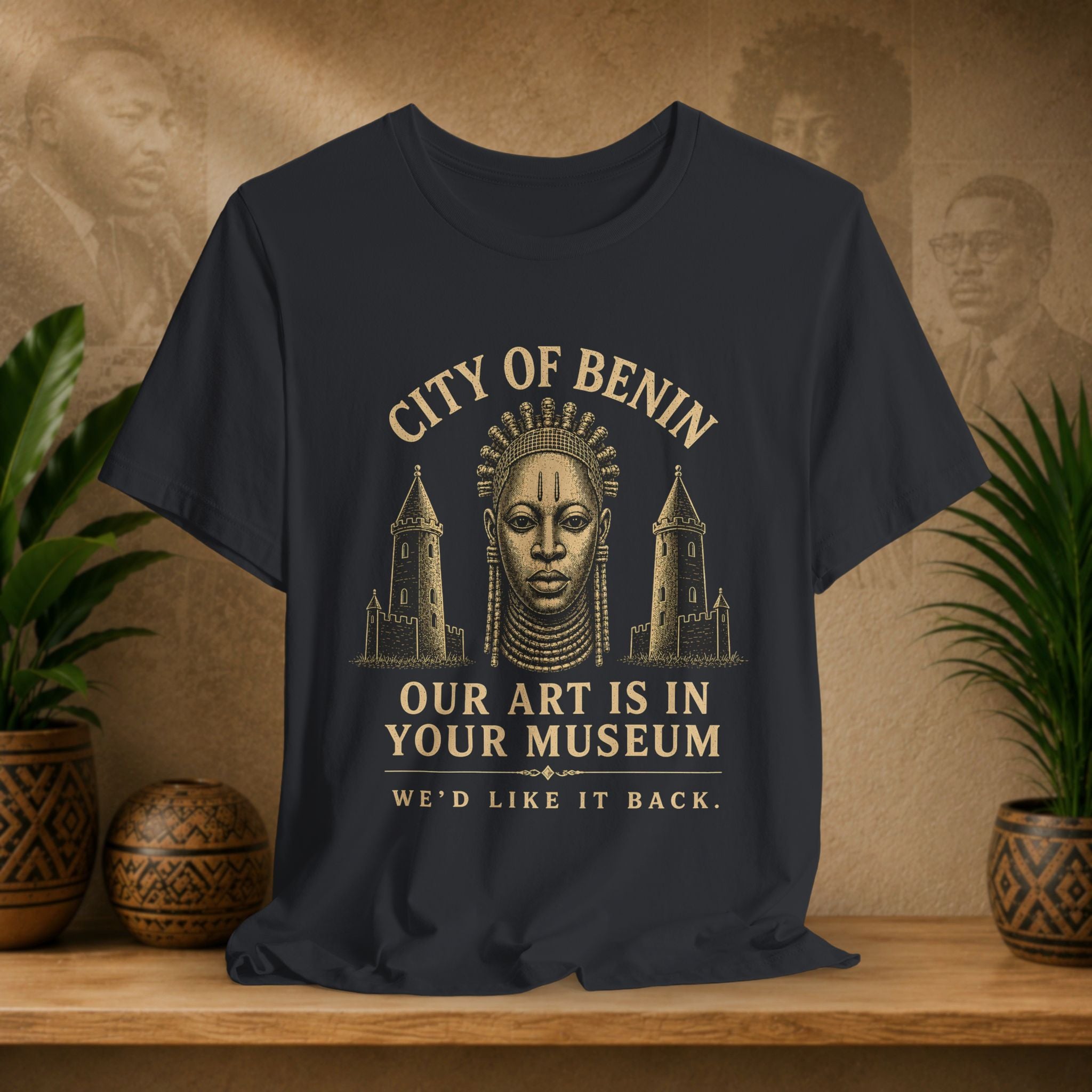 Black t-shirt with gold text and graphic of a face and towers on a wooden surface with plants and decorative items.