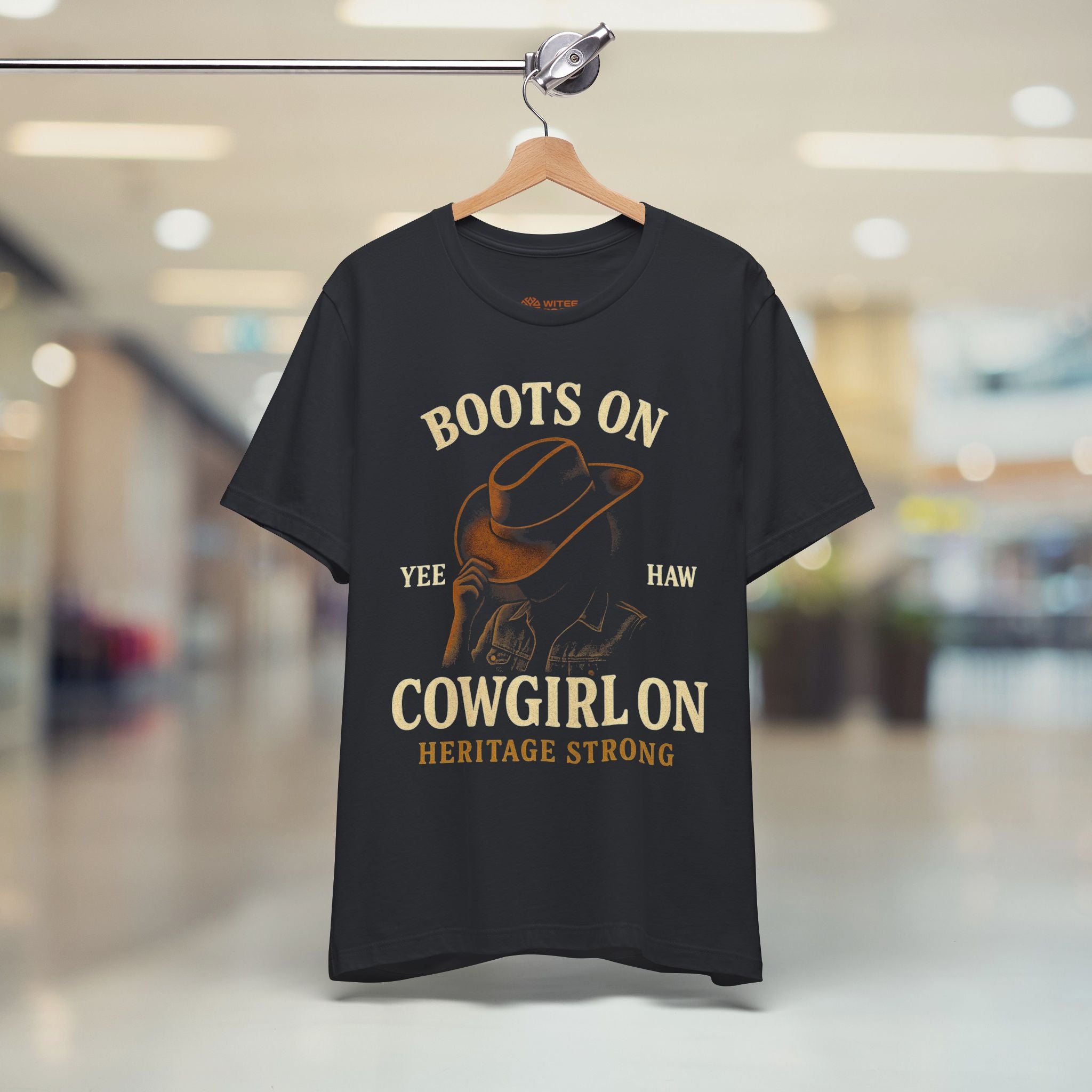 Black t-shirt with cowboy graphic and text on a hanger in a store setting
