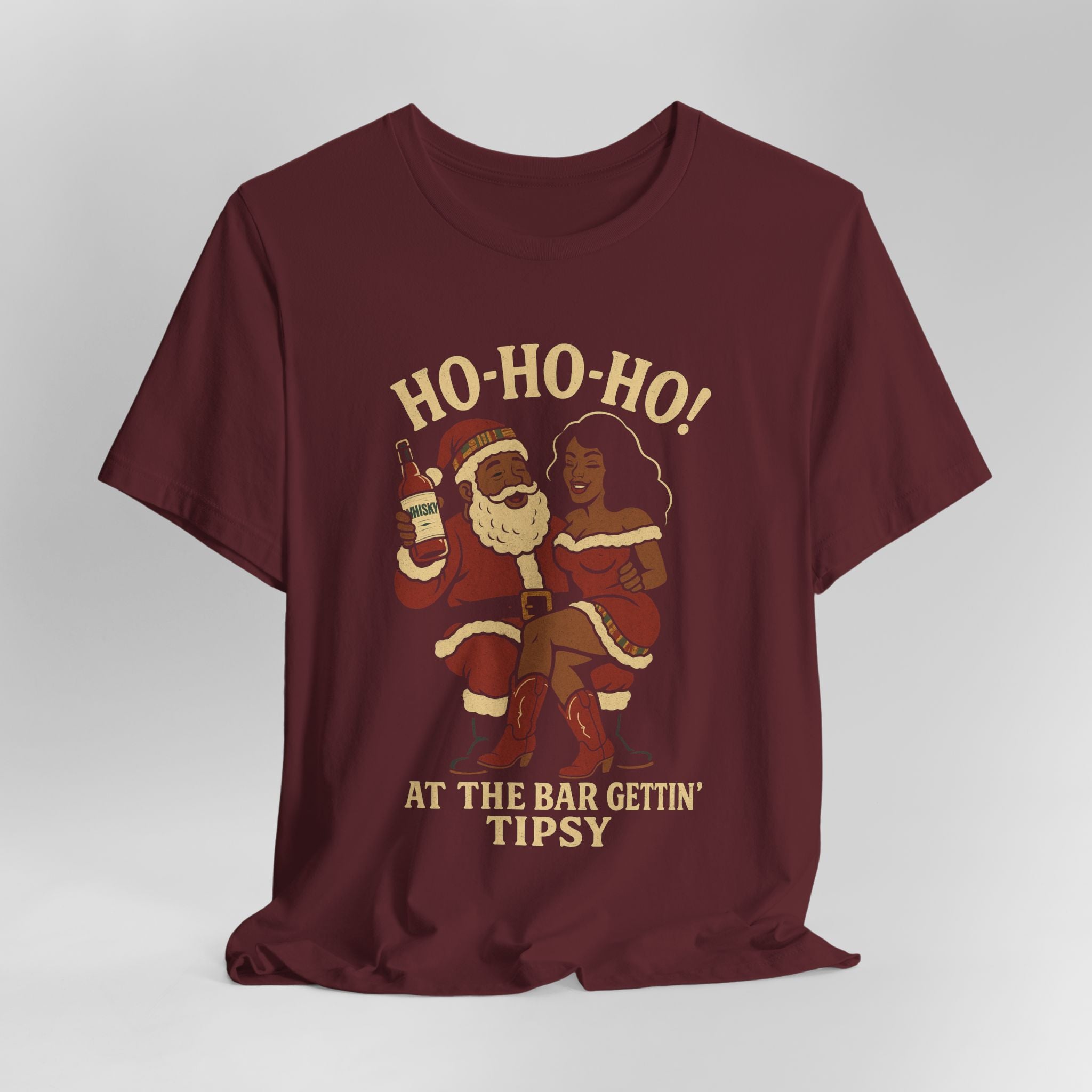 Maroon t-shirt with graphic of Santa and a woman holding drinks, text 'HO-HO-HO! AT THE BAR GETTIN' TIPSY' on a gray background.