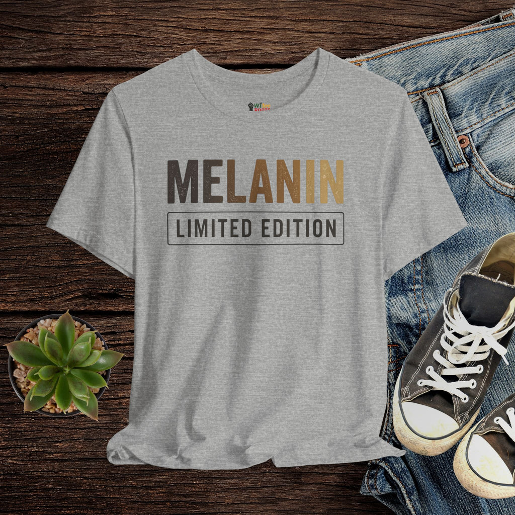 Gray t-shirt with 'MELANIN LIMITED EDITION' text on a wooden surface with jeans and sneakers.