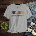Gray t-shirt with 'MELANIN LIMITED EDITION' text on a wooden surface with jeans and sneakers.
