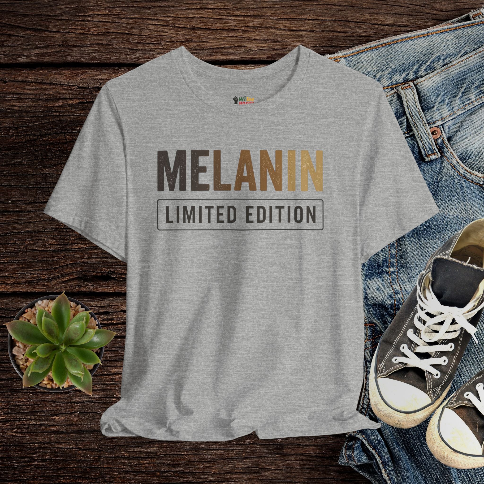 Gray t-shirt with 'MELANIN LIMITED EDITION' text on a wooden surface with jeans and sneakers.