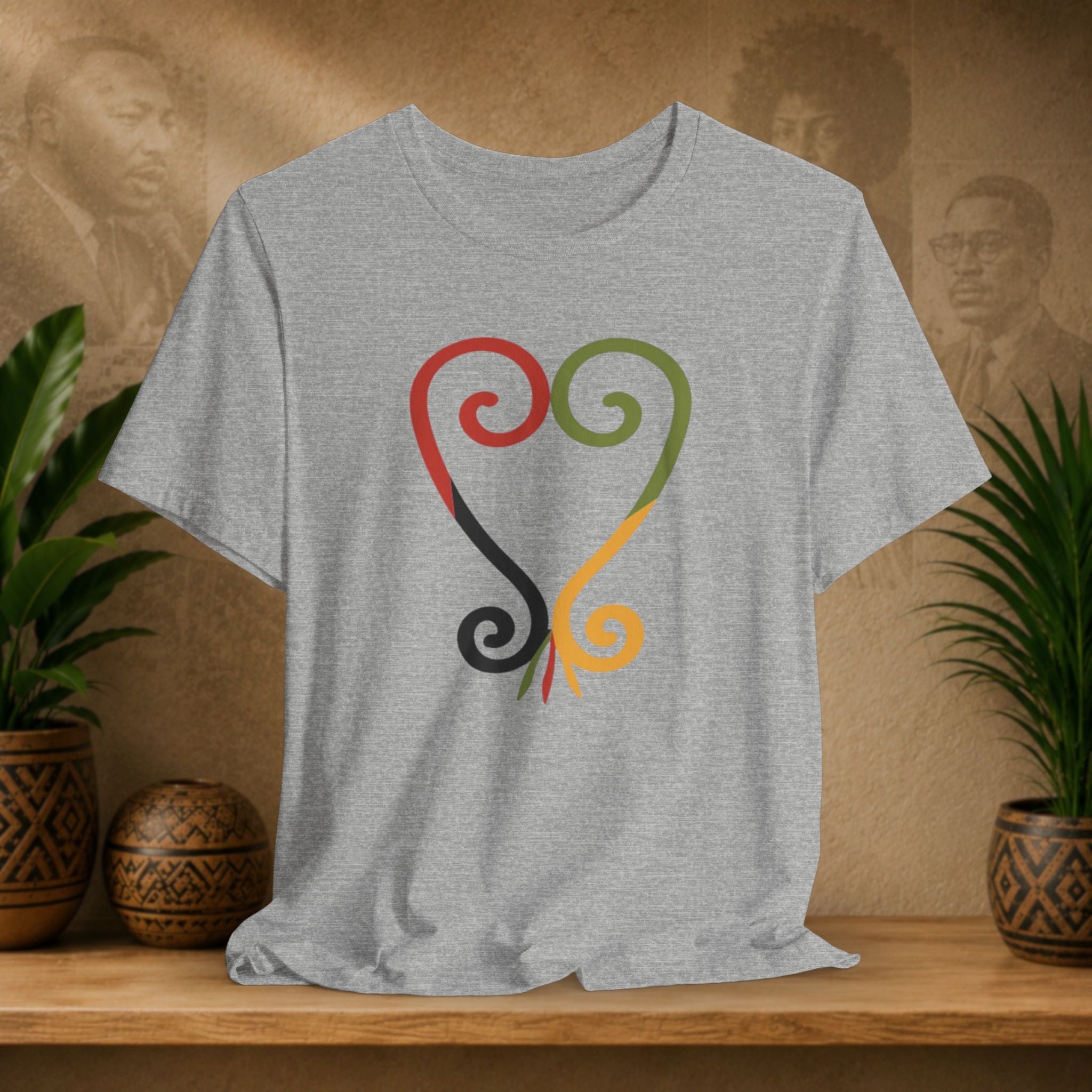 Gray t-shirt with colorful abstract design on a wooden surface with plants and a textured wall background