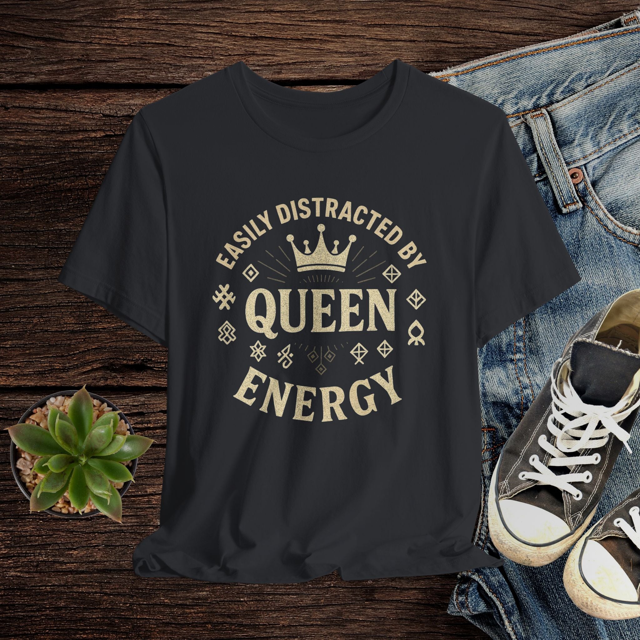 Black t-shirt with 'Easily Distracted by Queen Energy' text on a wooden surface with jeans and sneakers.