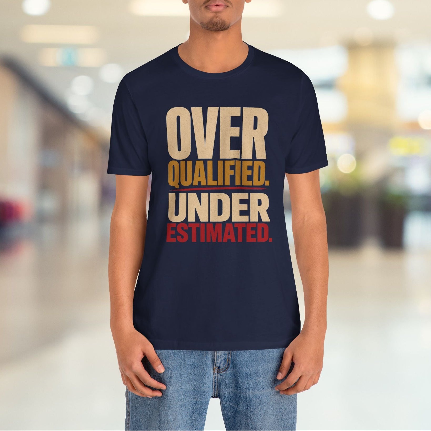 A man wearing a navy blue graphic t-shirt with the text 'OVER QUALIFIED. UNDER ESTIMATED.