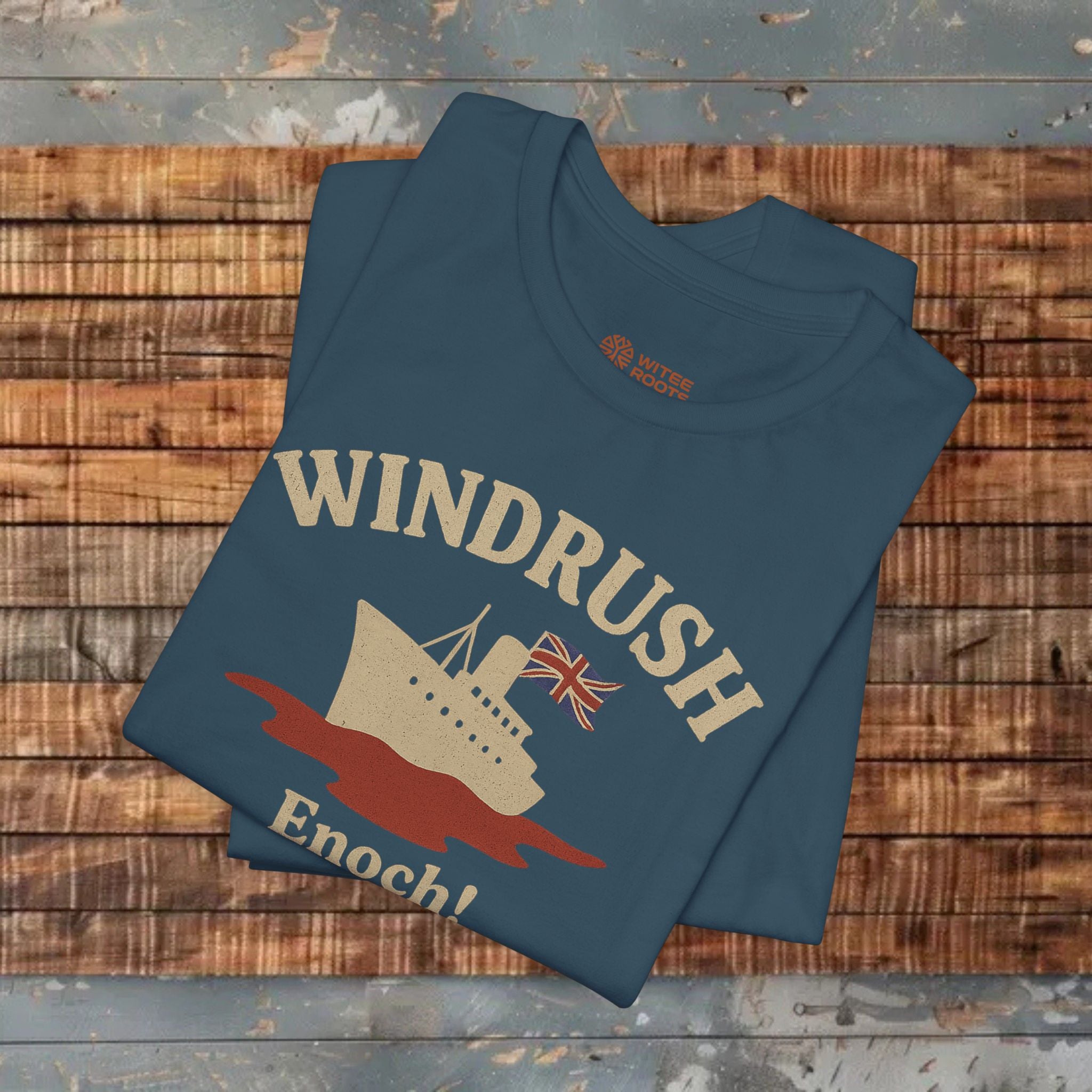 Folded blue t-shirt with 'Windrush Enoch!' design on a wooden surface