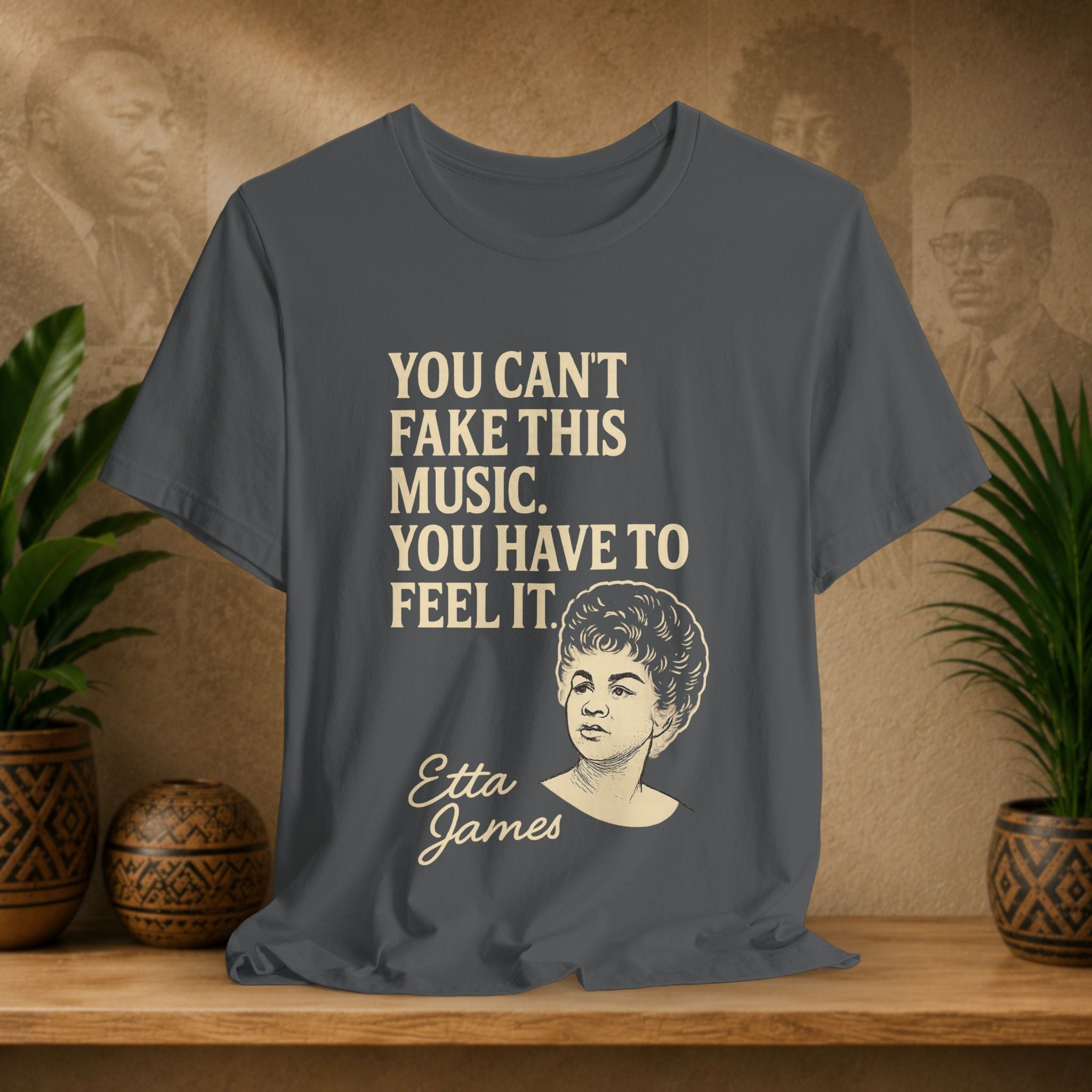 Gray t-shirt with Etta James quote on a wooden surface with plants and wall art in the background