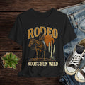 Black t-shirt with cowboy graphic and 'Rodeo Roots Run Wild' text on a wooden surface with jeans and sneakers.