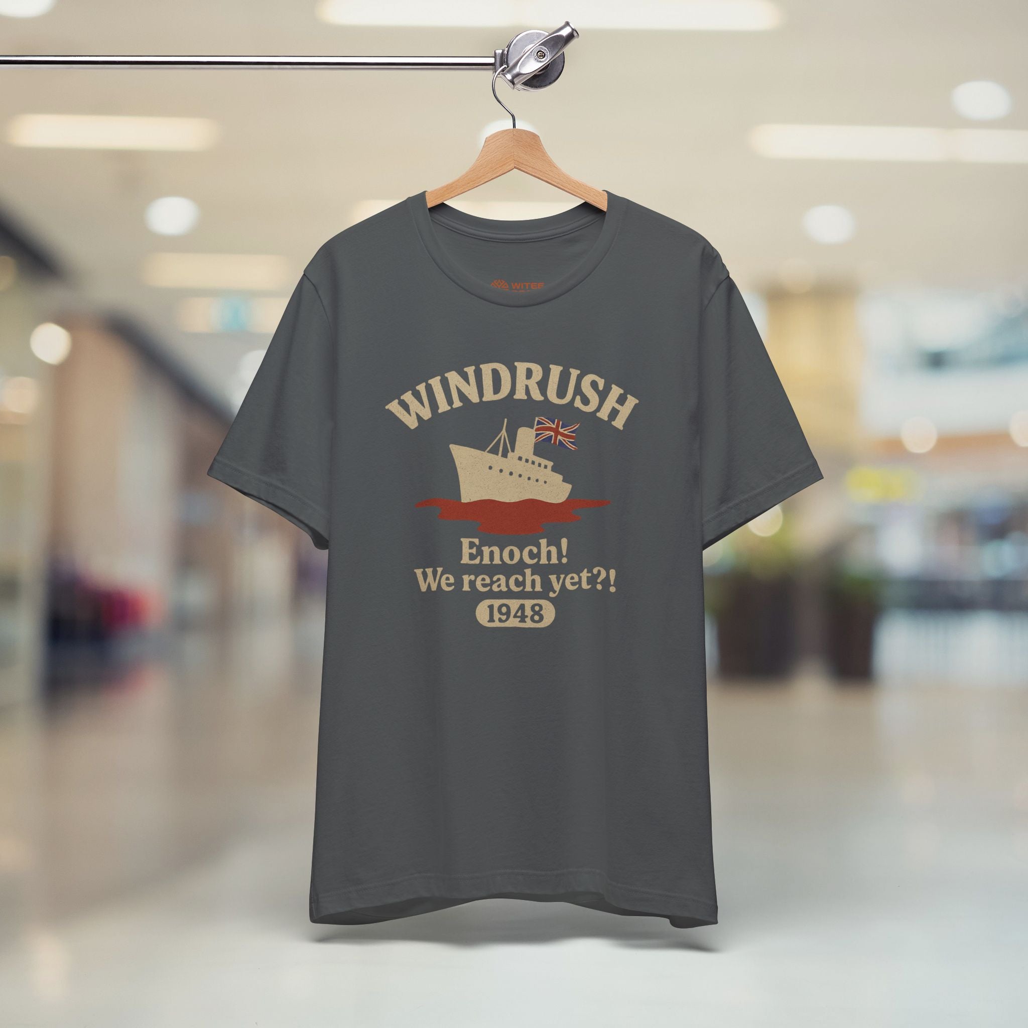Gray t-shirt with 'Windrush' design on a hanger in a store.