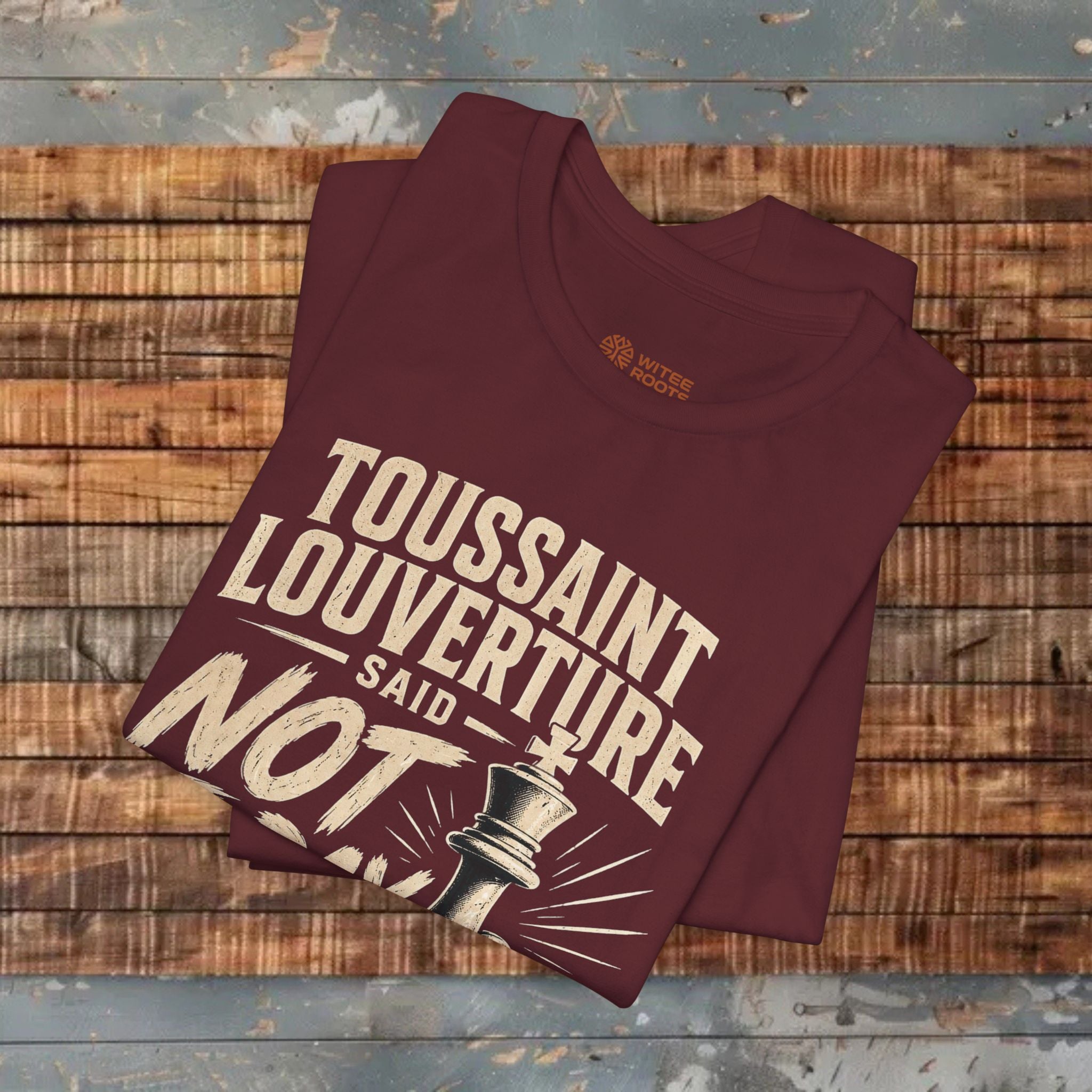Folded maroon t-shirt with text and graphic on a wooden surface