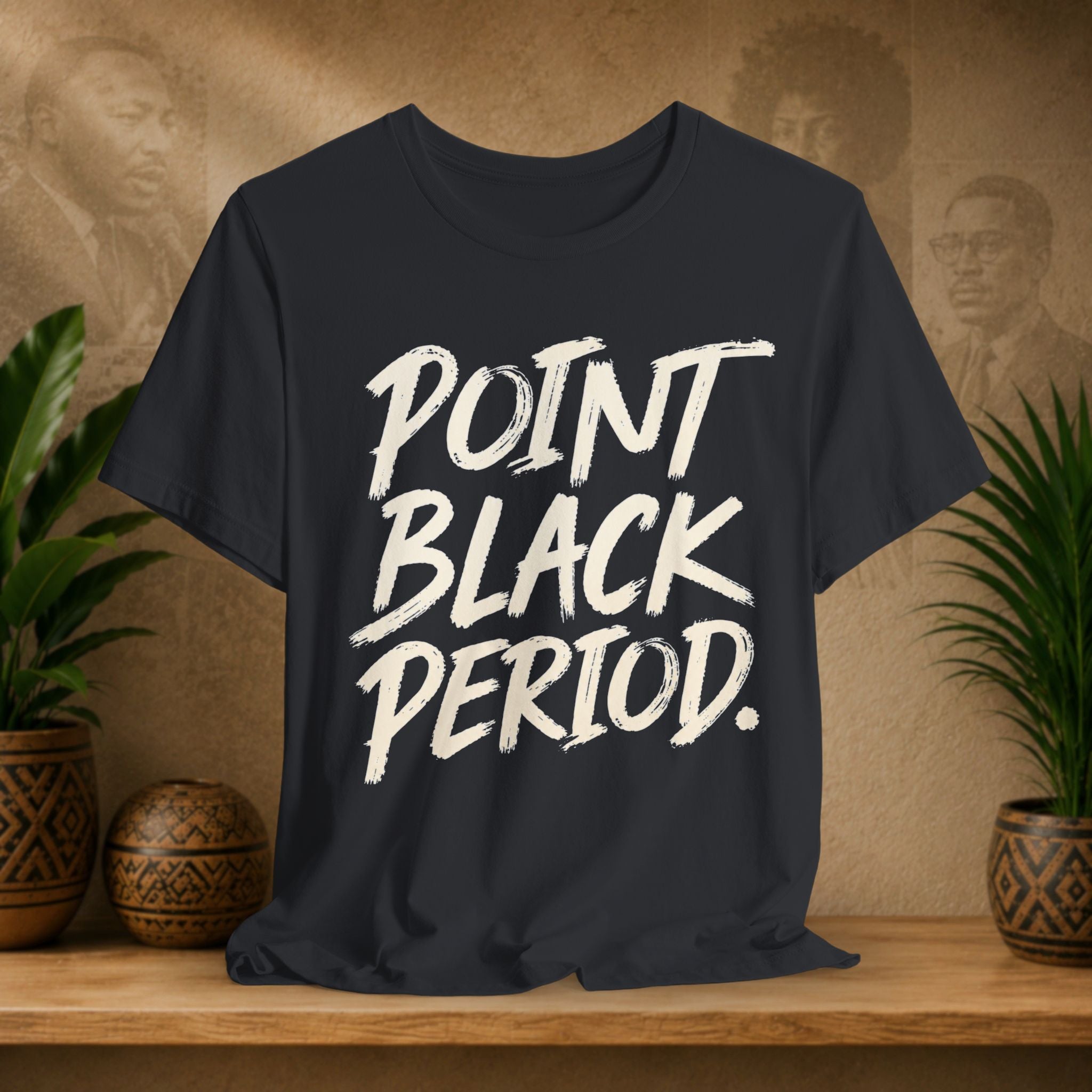 Black t-shirt with the text 'POINT BLACK PERIOD.' printed in a distressed white brush font, displayed on a wooden shelf with potted plants and a textured background.