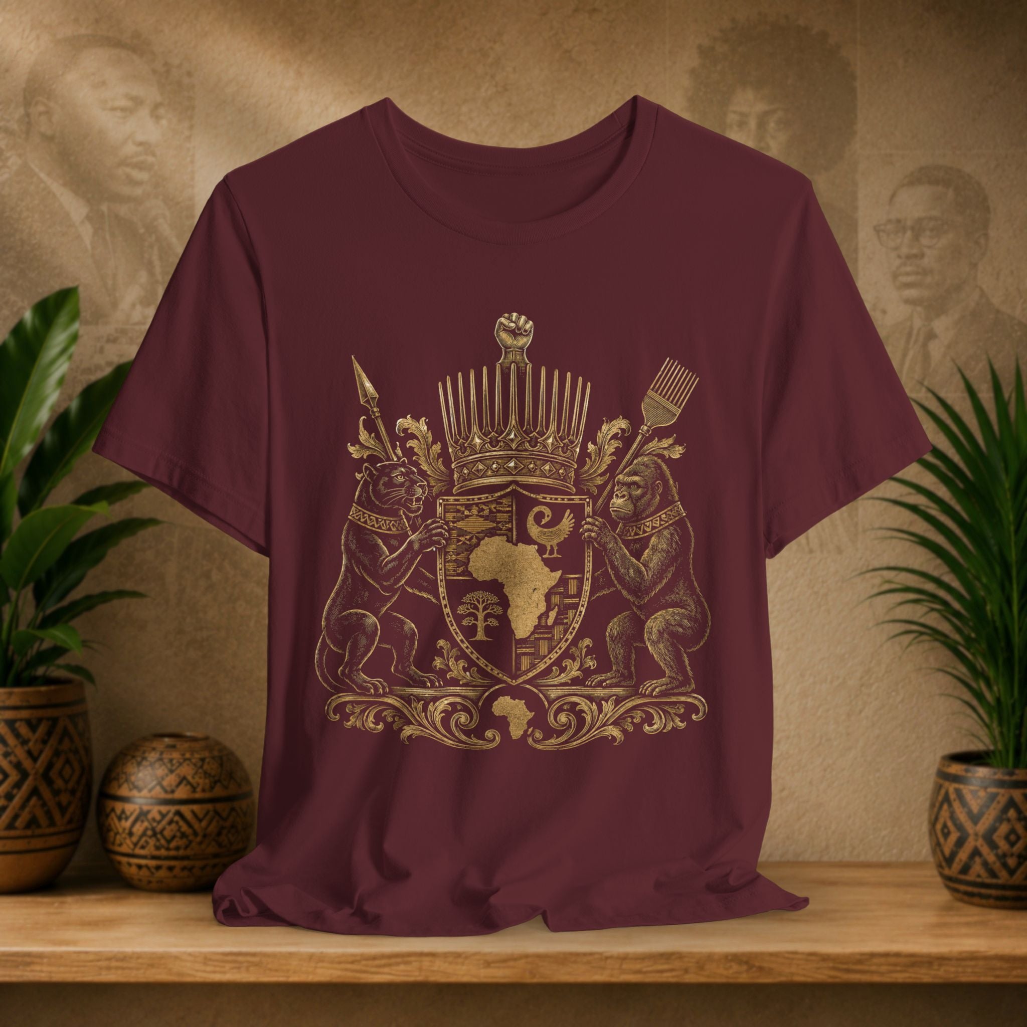 Maroon t-shirt with gold emblem featuring African design on a wooden surface with plants and decorative items.