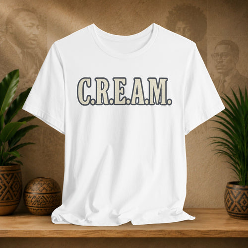 White t-shirt with 'C.R.E.A.M.' text on a wooden shelf with plants and a textured wall background