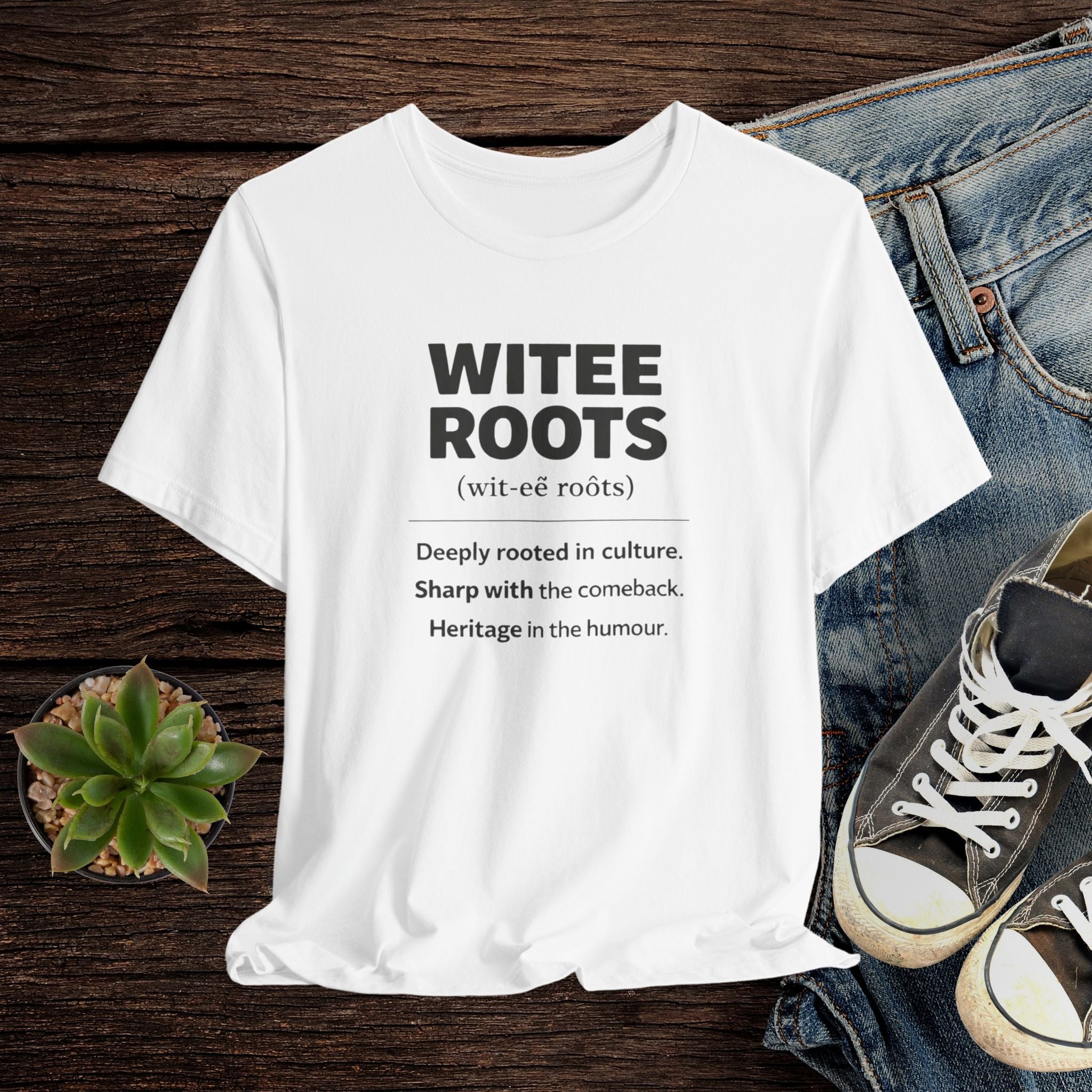 White t-shirt with 'WITEE ROOTS' text on a wooden surface with jeans and sneakers.
