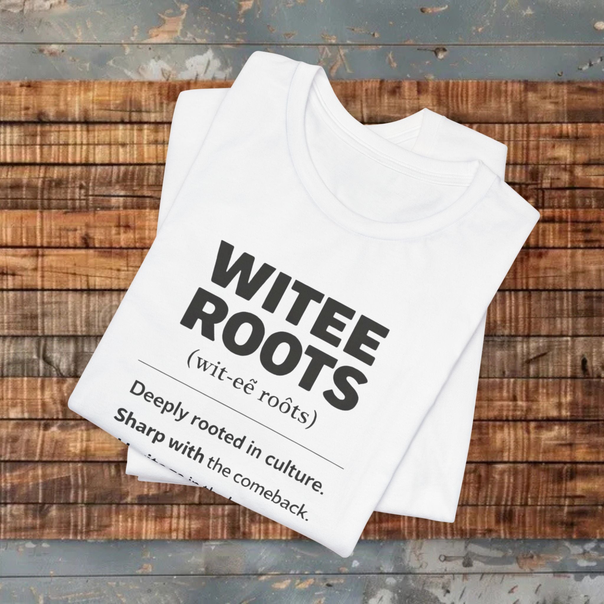 White t-shirt with 'WITEE ROOTS' text on a wooden surface