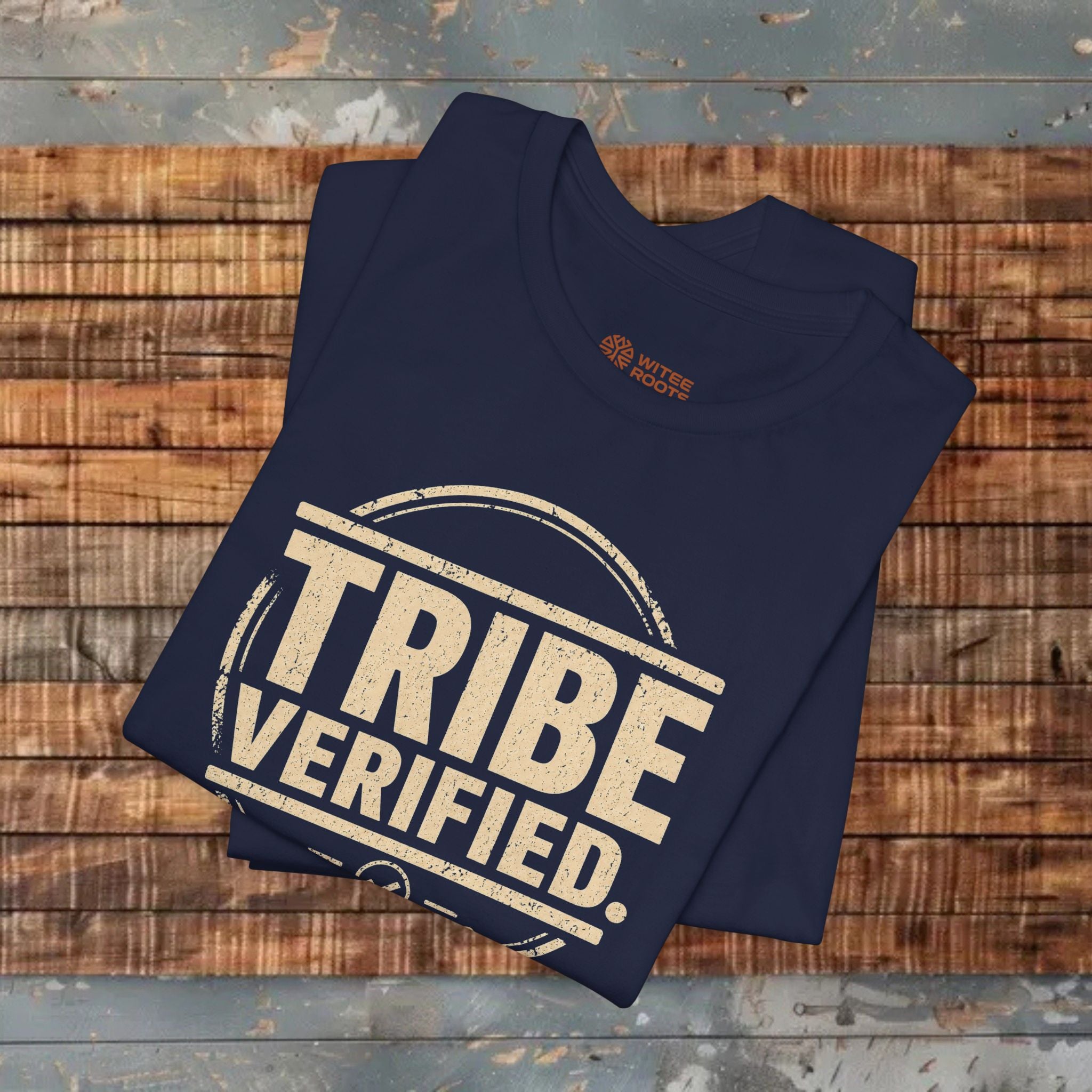 Folded navy blue t-shirt with 'TRIBE VERIFIED' text on a wooden surface
