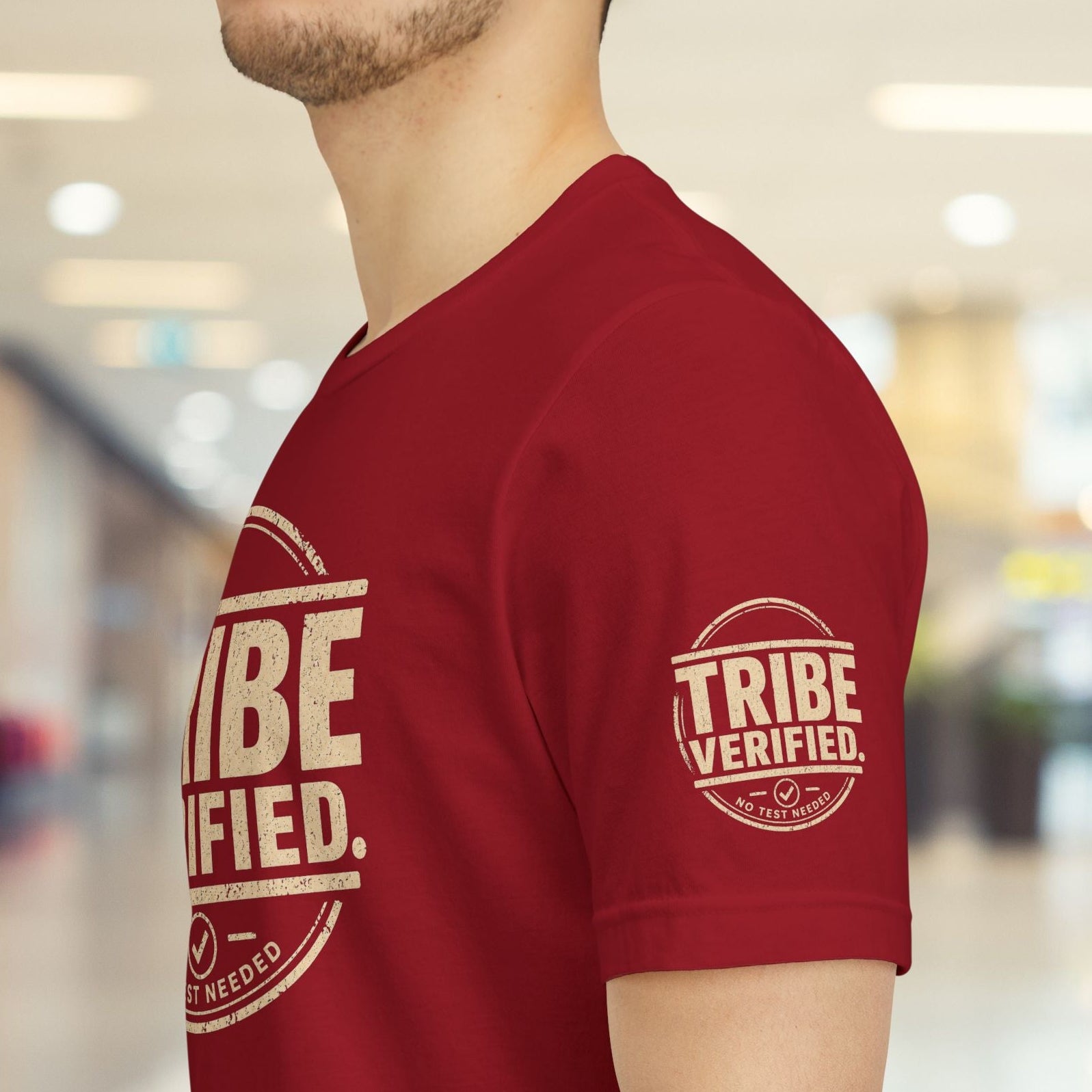 Person wearing a red t-shirt with 'TRIBE VERIFIED' text in a blurred indoor setting