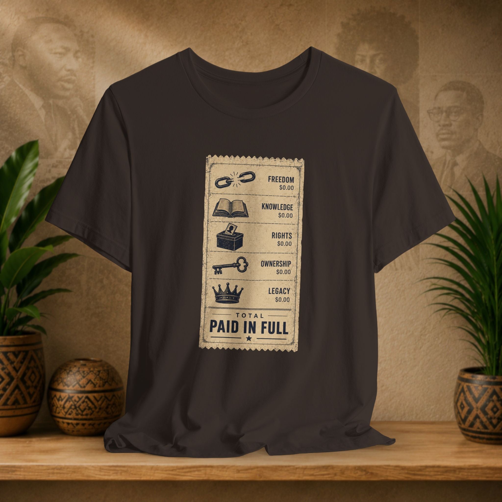 Brown t-shirt with a graphic design on a wooden surface with plants and a textured wall in the background