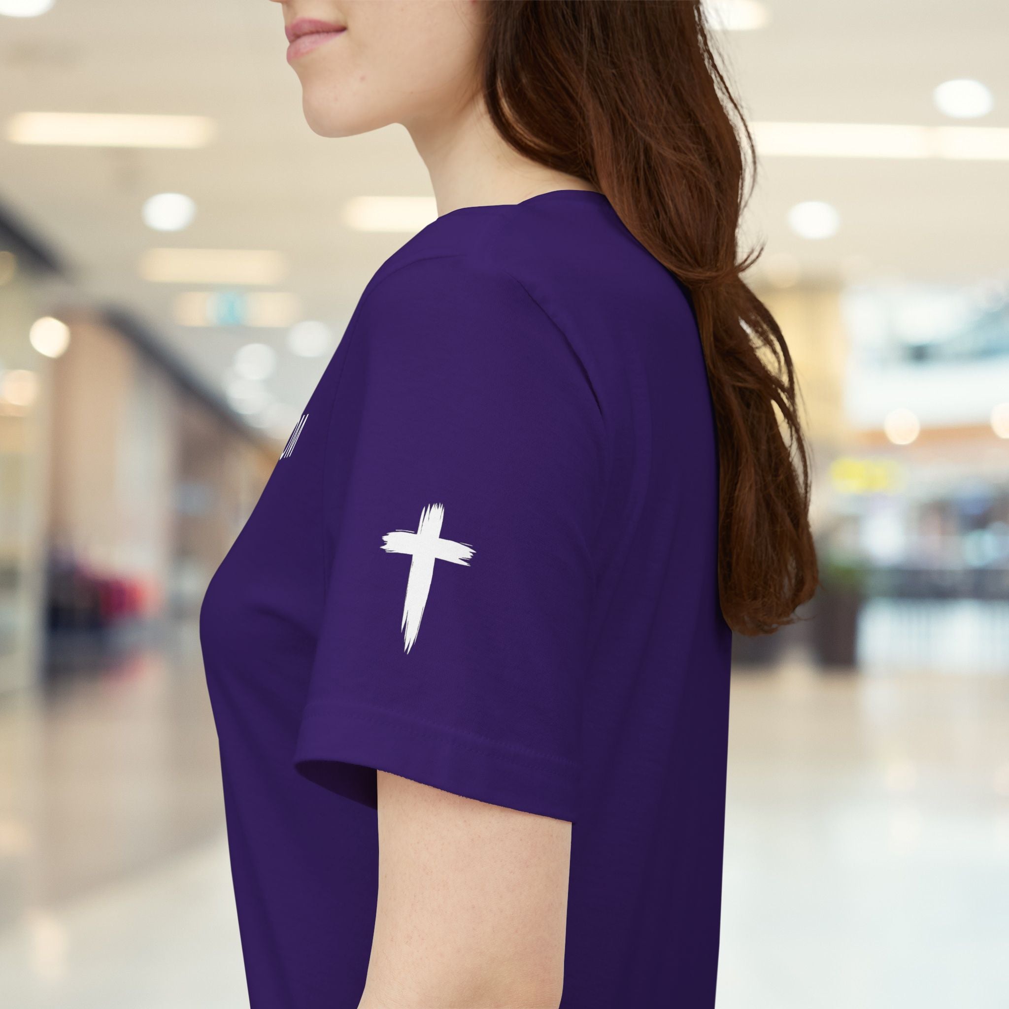 Person wearing a purple t-shirt with a white cross design in a blurred indoor setting