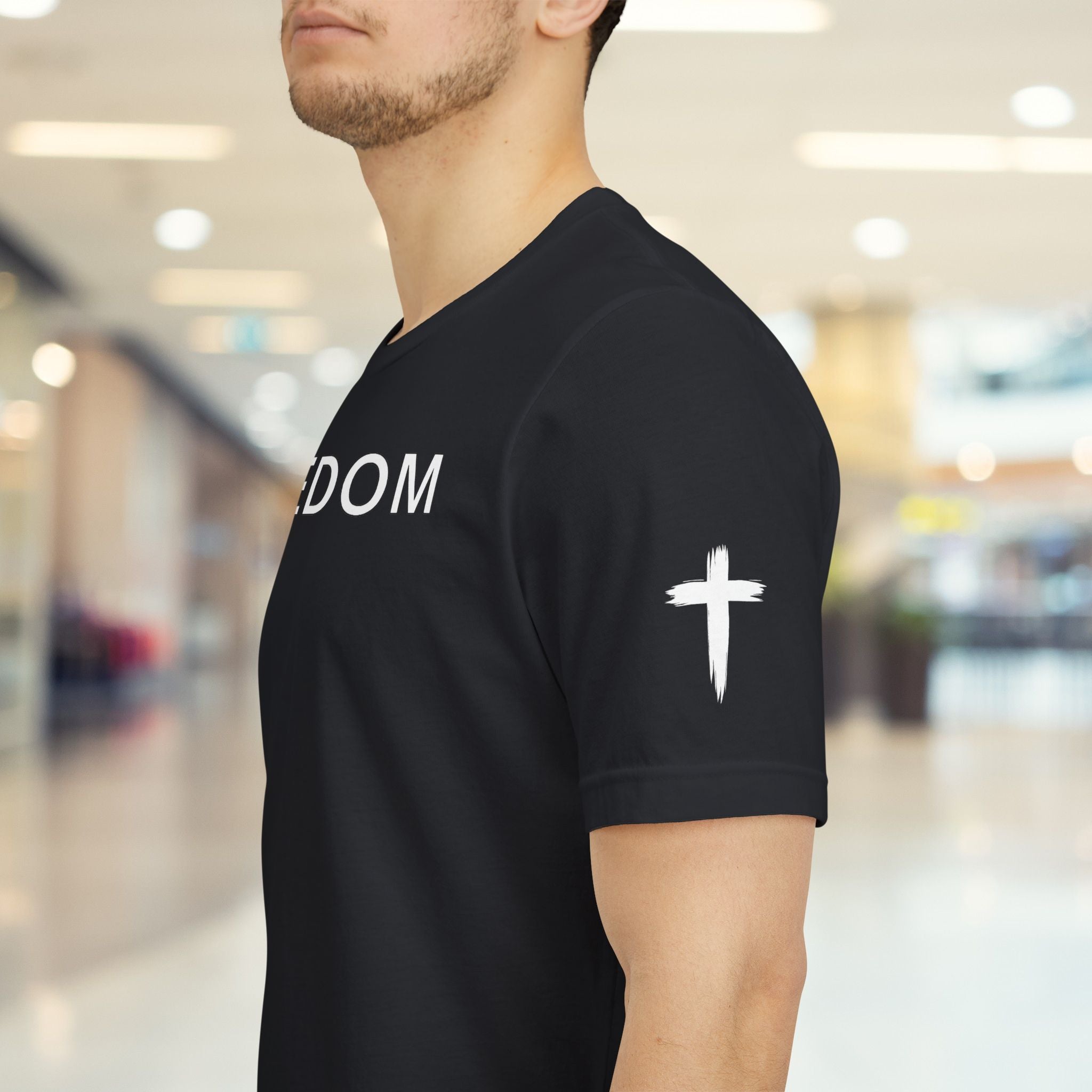 Person wearing a black t-shirt with 'DOM' text and a white cross on the sleeve in a blurred indoor setting.