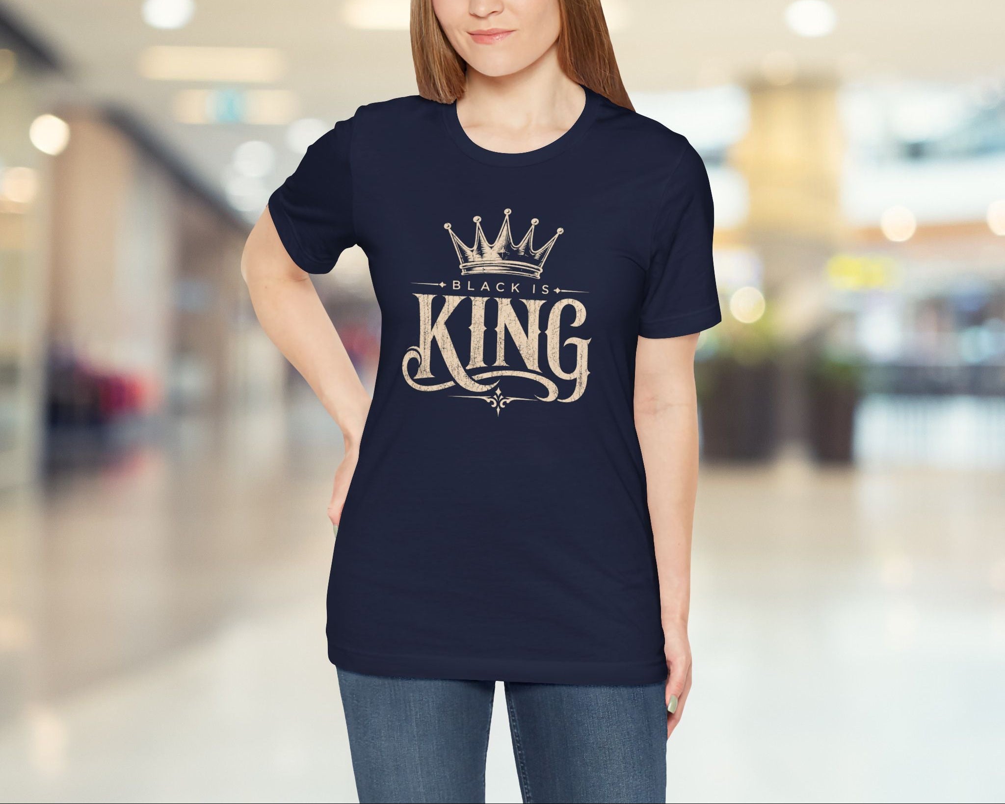 Woman wearing a navy blue t-shirt with 'Black is King' text in a mall.