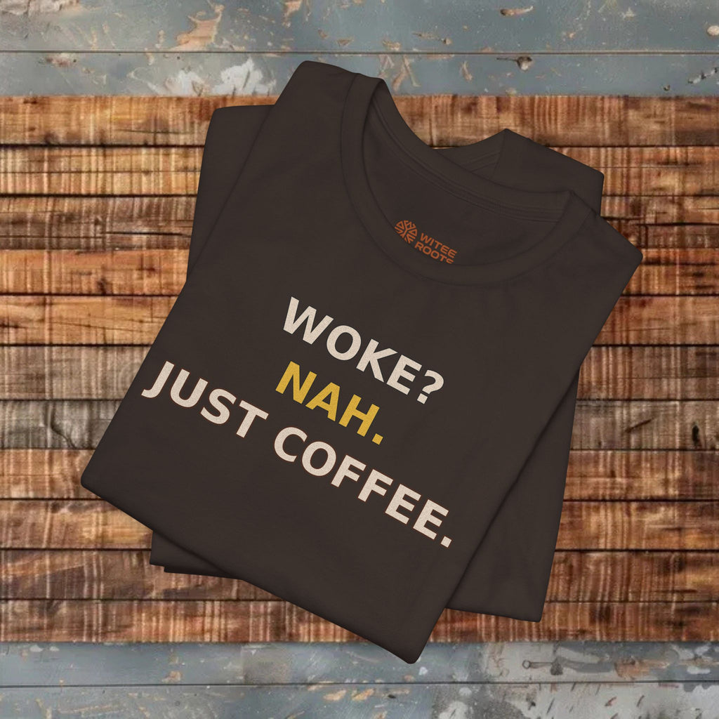 Folded black t-shirt with 'WOKE? NAH. JUST COFFEE.' text on a wooden surface