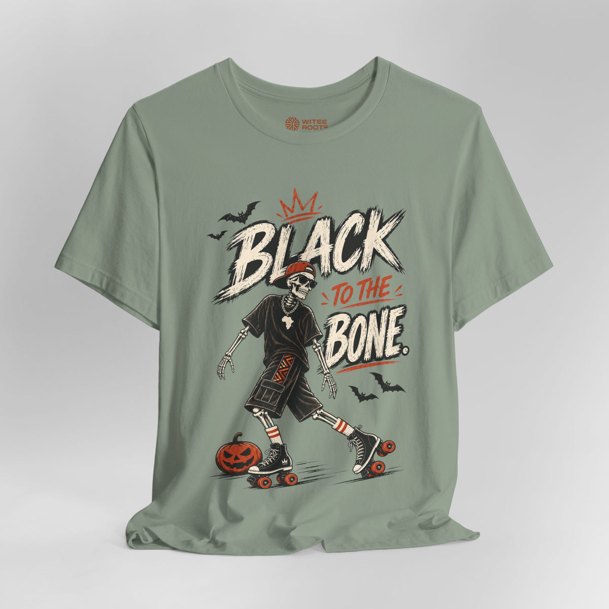 A sage green graphic t-shirt featuring a skeleton roller skate design with the text 'BLACK TO THE BONE' and small bats, shown on a neutral gray background.